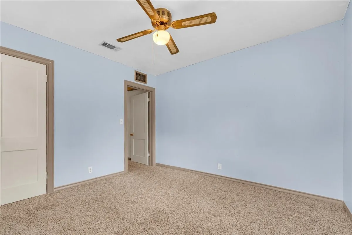 Carpeted room featuring light blue walls, a ceiling fan with light fixture, and two panel doors with contrasting trim