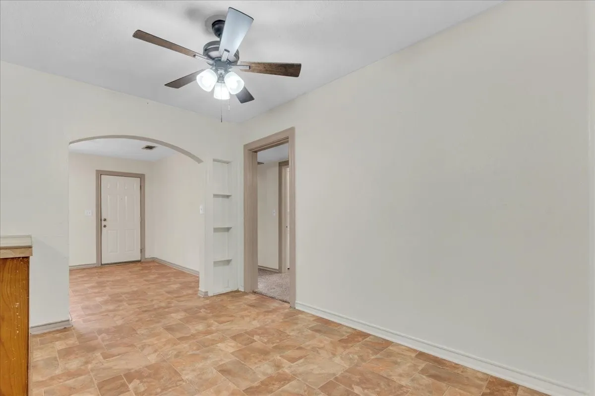 Neutral wall paint, patterned floor tiling, an arched doorway, and a ceiling fan with light fixture