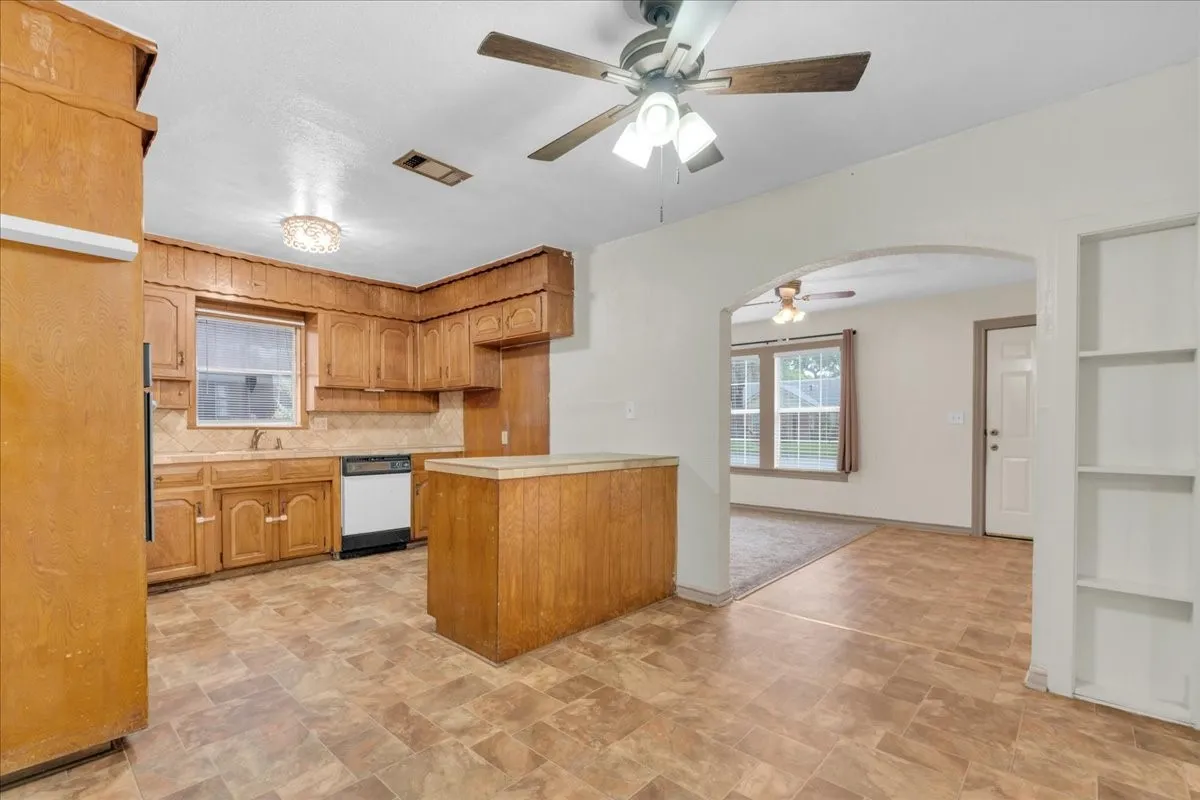 Kitchen featuring wood cabinetry, a built-in dishwasher, tile backsplash, and an island with a contrasting countertop