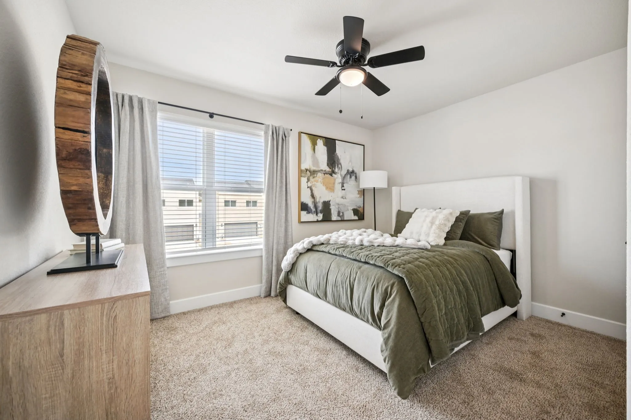 Bedroom featuring a wide window with blinds and drapes, a ceiling fan with integrated lighting, clean white walls, and plush carpet flooring