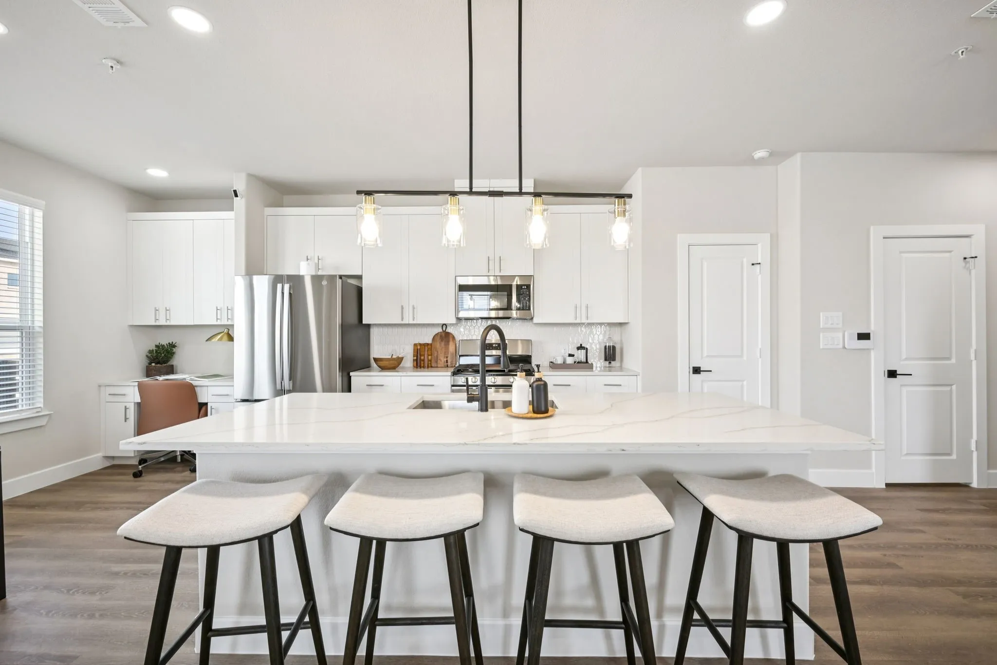Spacious kitchen featuring a large central island with seating, stainless steel appliances, white cabinetry, and wood-finish flooring