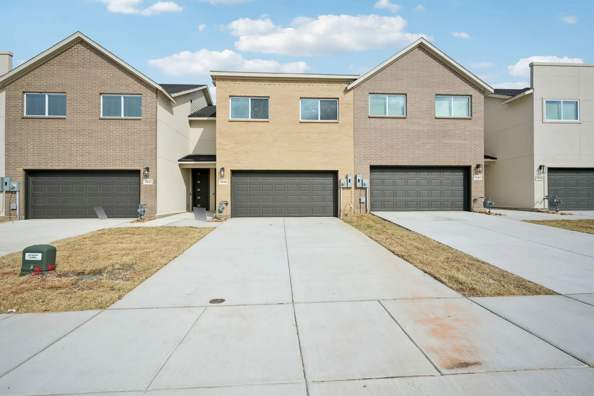 Contemporary townhomes featuring a brick facade, integrated two-car garages, and concrete driveways
