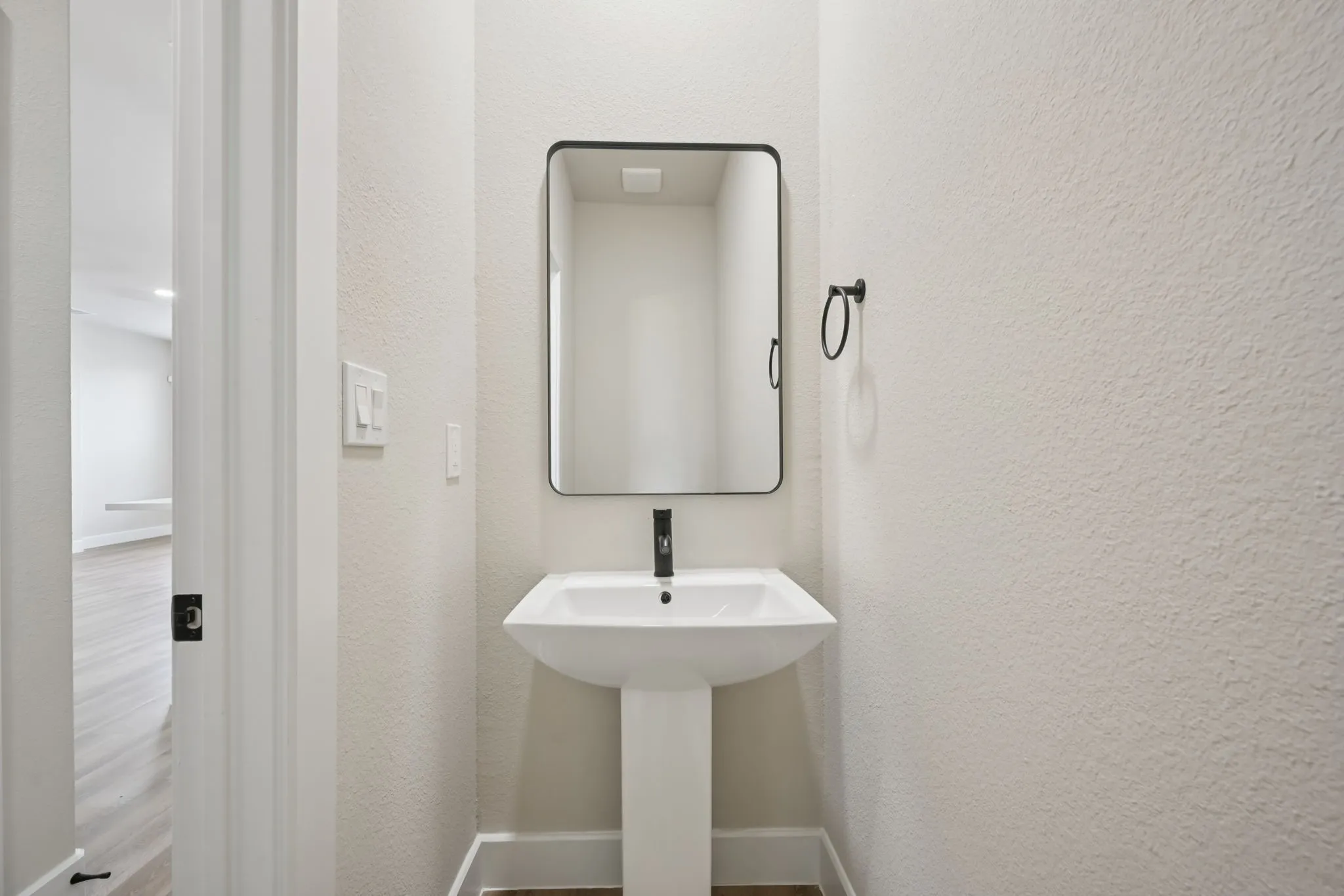 Pedestal sink with matte black faucet, framed mirror, and towel ring