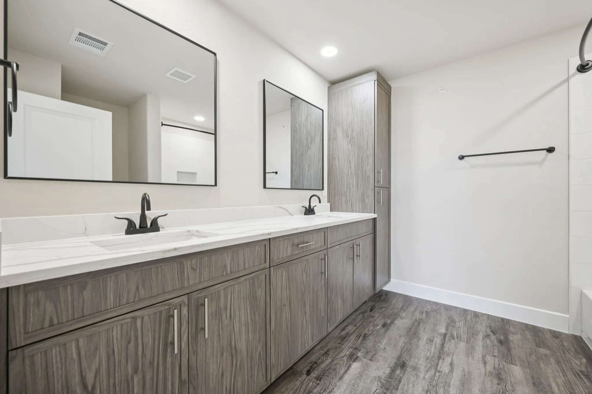 Dual vanity with white countertops and matte black fixtures, set against wood-finish flooring