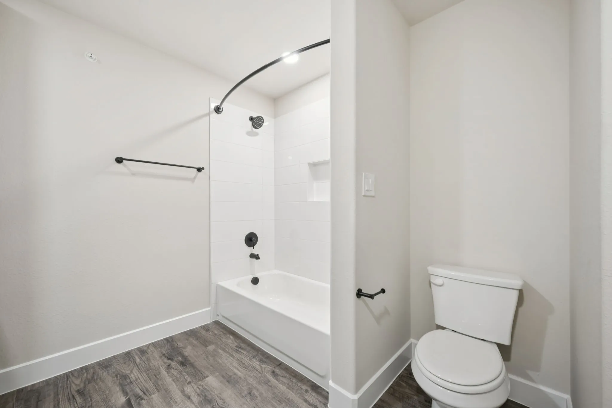 Bathroom featuring a white bathtub with subway tile surround, matte black fixtures, and a recessed shower niche