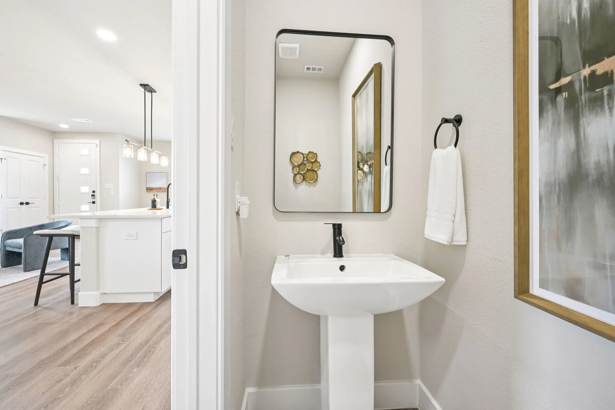 Pedestal sink with matte black faucet, framed mirror, and wood-finish flooring
