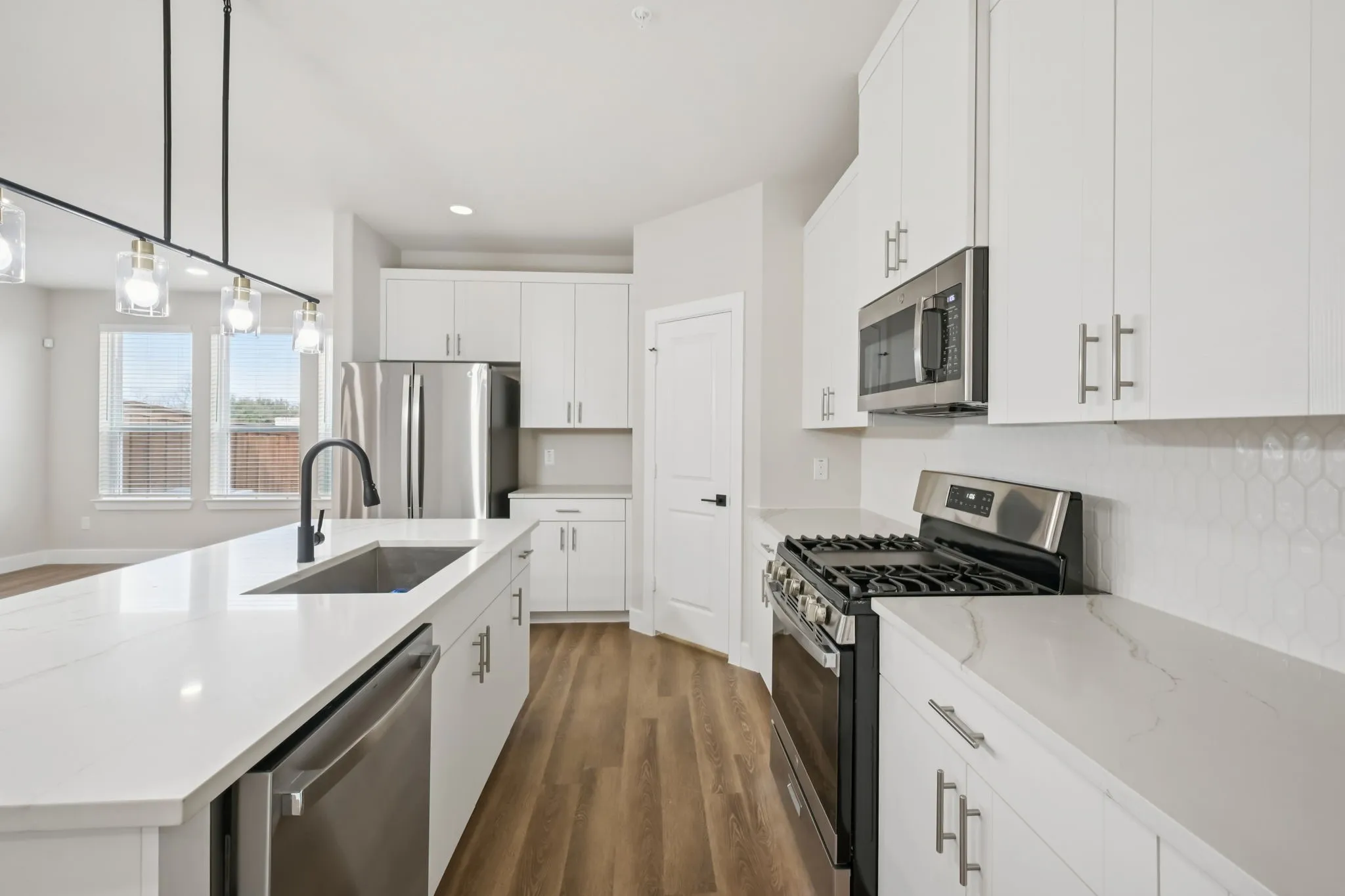 Spacious kitchen featuring white cabinetry, integrated stainless steel appliances, a large island with an undermount sink, a matte black faucet, and durable wood-finish flooring