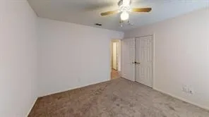 Carpeted room featuring a ceiling fan with light fixture, white walls, and bi-fold closet doors