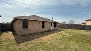 Expansive rear yard featuring a wooden privacy fence, a brick exterior with multiple windows, and a prominent chimney