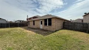 Fenced backyard featuring a brick exterior, single-panel door, and two windows