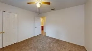 Carpeted room featuring a ceiling fan with light fixture, white walls, and bi-fold closet doors with brass hardware