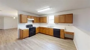 Kitchen featuring wood-finish flooring, a full suite of black appliances, wood cabinetry, light countertops, and a double basin sink