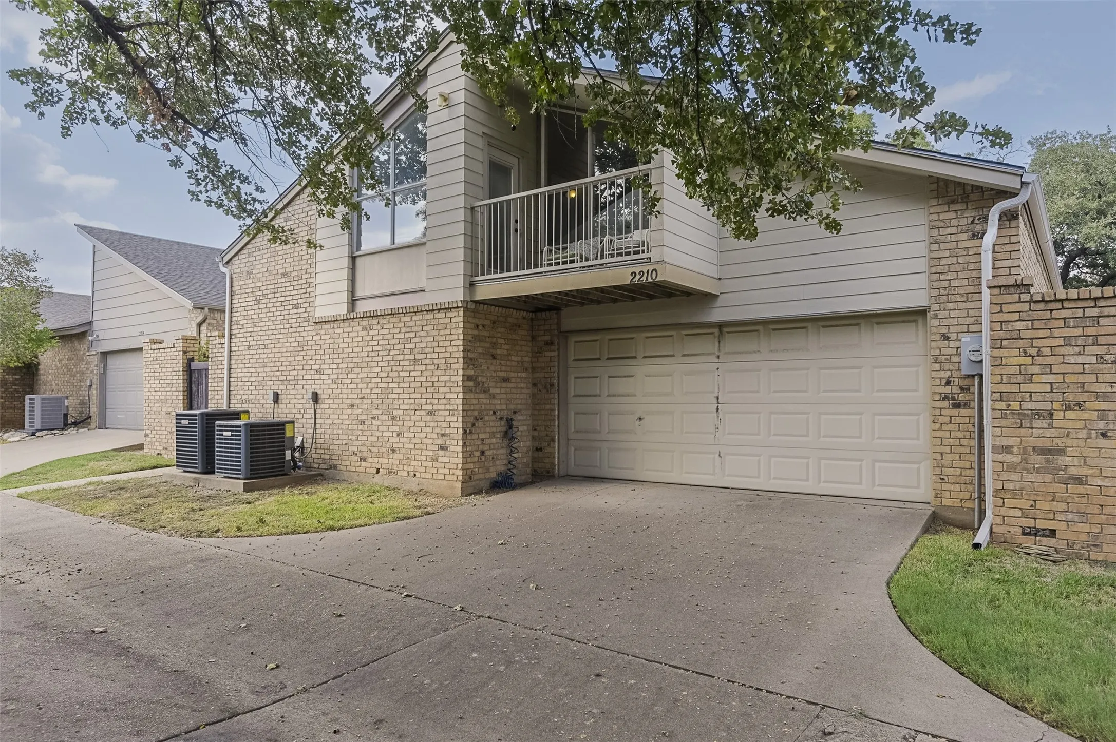 Brick and siding exterior with an attached garage, upper-level balcony, and gabled roofline