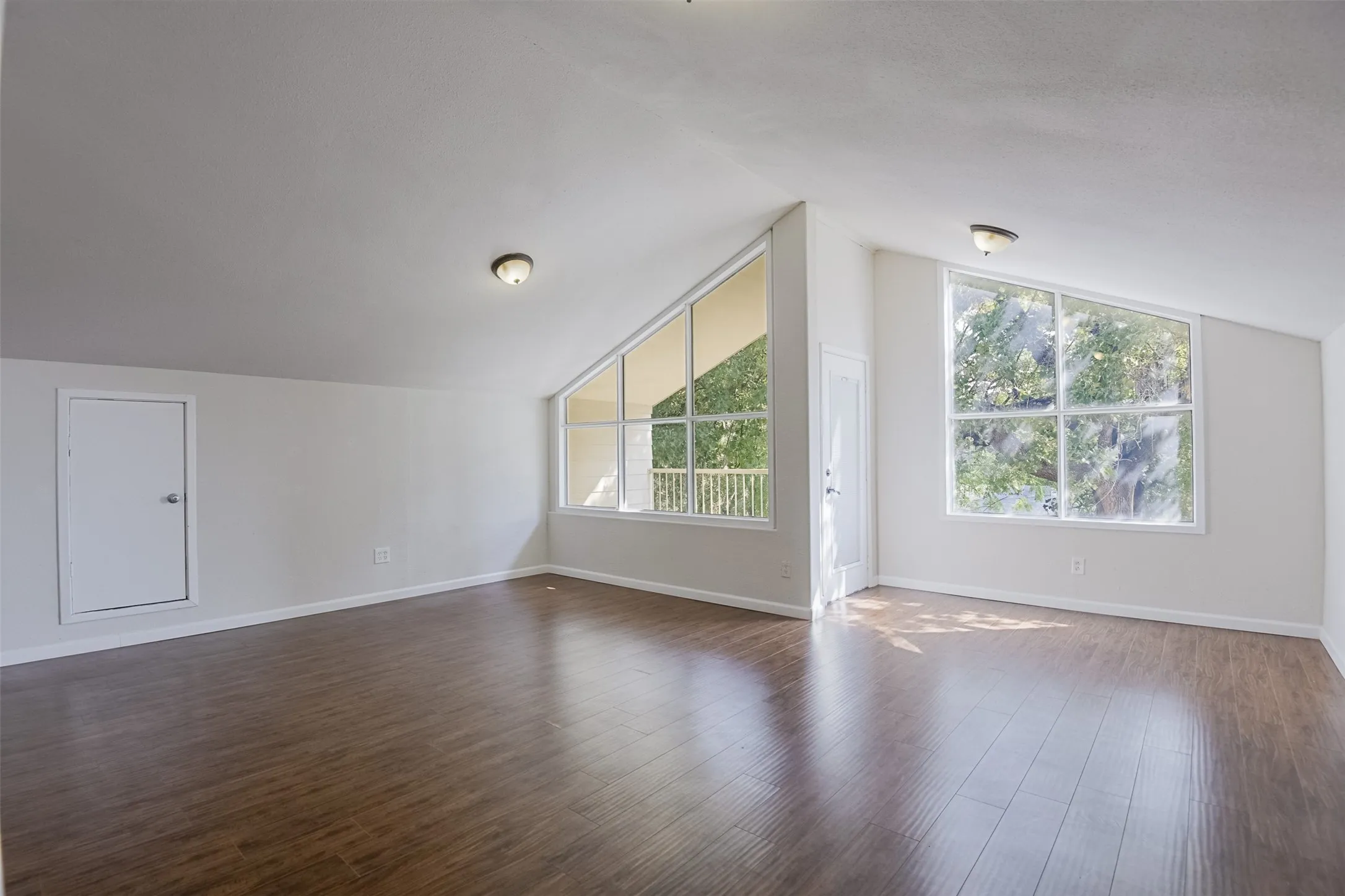 Vaulted ceilings, wood-finish flooring, two large multi-pane windows, and two flush-mount ceiling lights