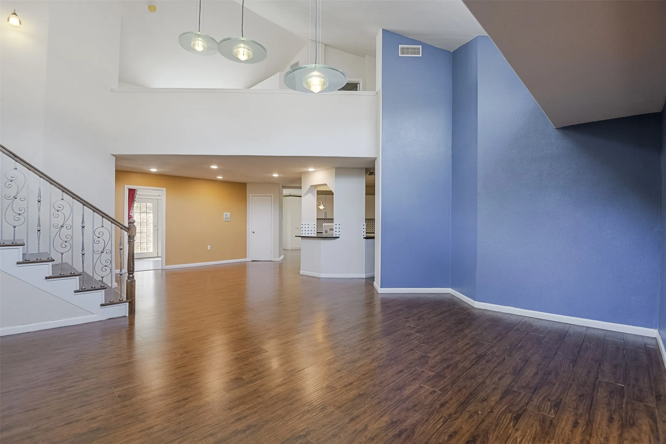 Open-concept living space featuring soaring ceilings with pendant lighting, rich wood-finish flooring throughout, and accent wall detailing in blue