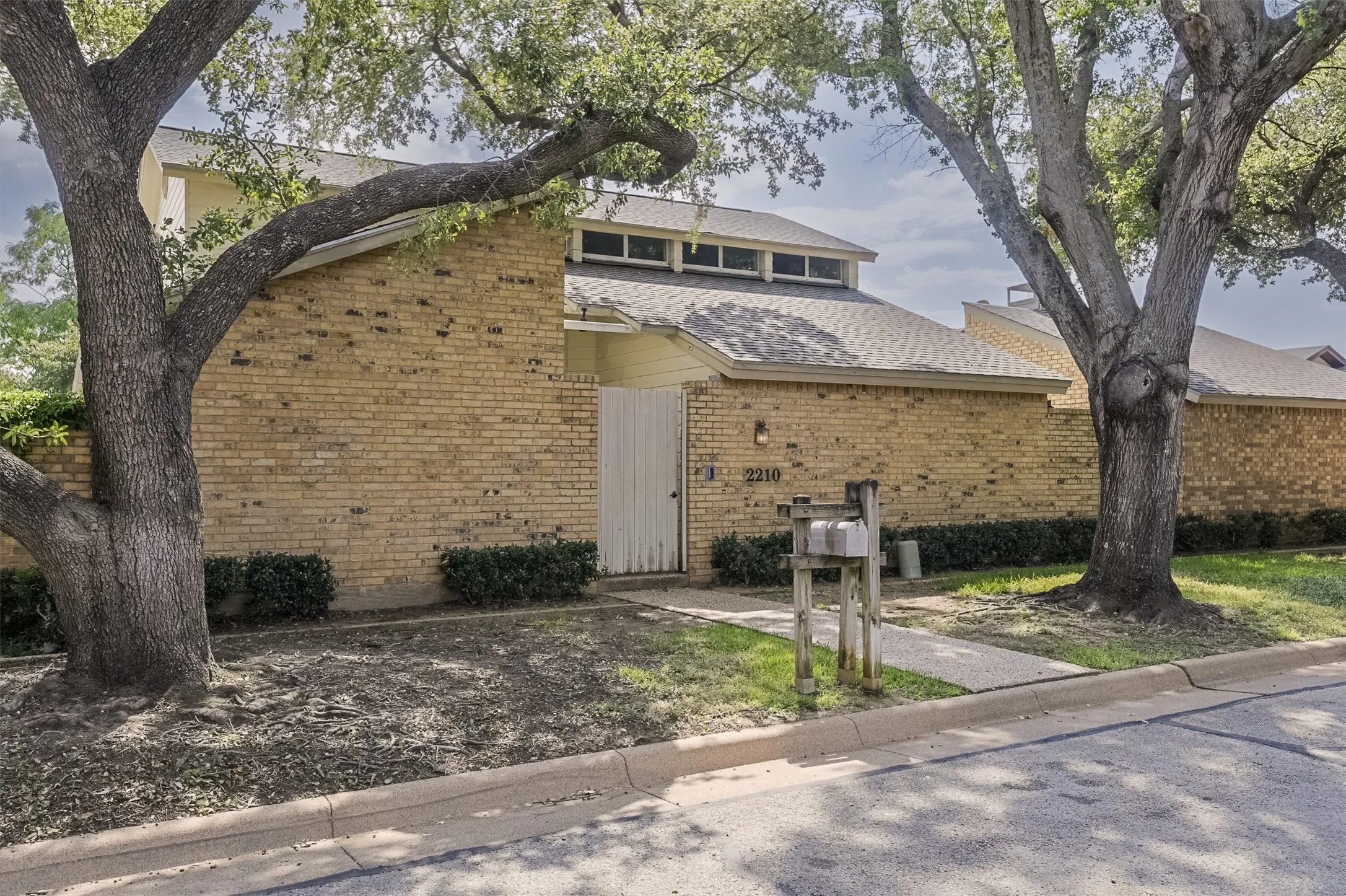 Brick exterior with a peaked roofline, front privacy fence, and integrated clerestory windows