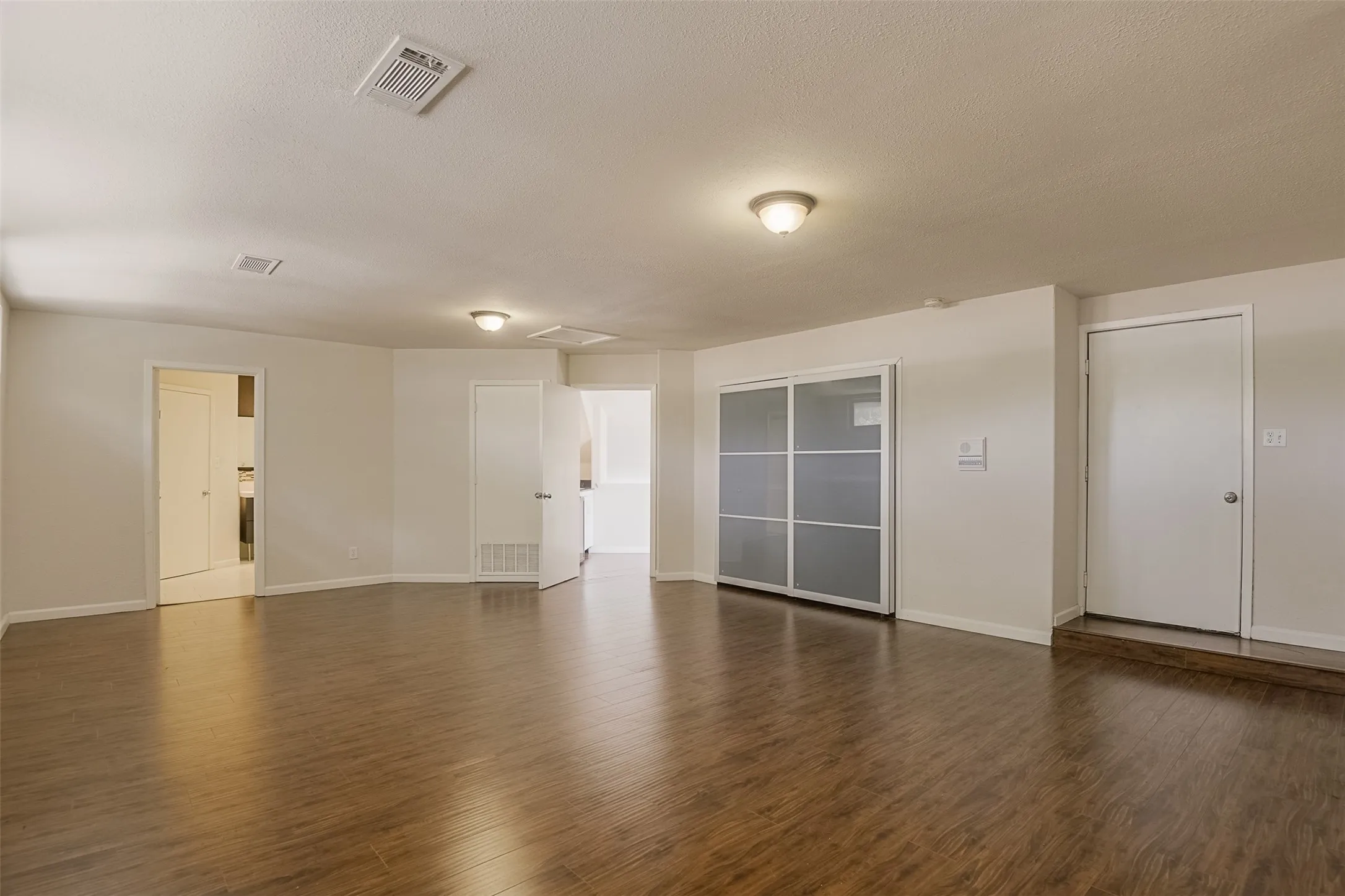 Wood-finish flooring throughout, white painted walls, ceiling-mounted light fixtures, and a sliding door closet with opaque panels