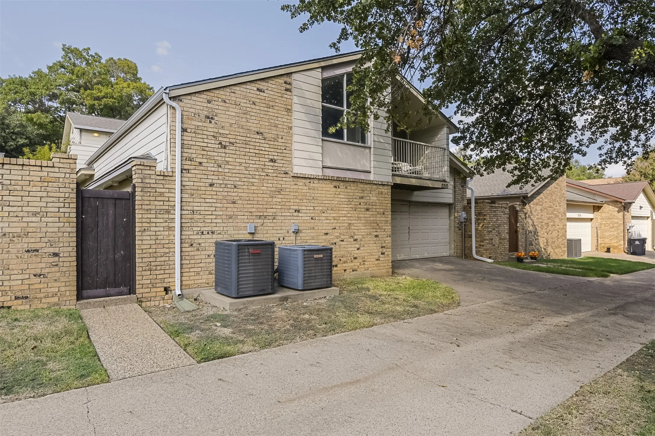 Brick exterior with siding accents, attached garage, second-story balcony with railings, and a side entry gate