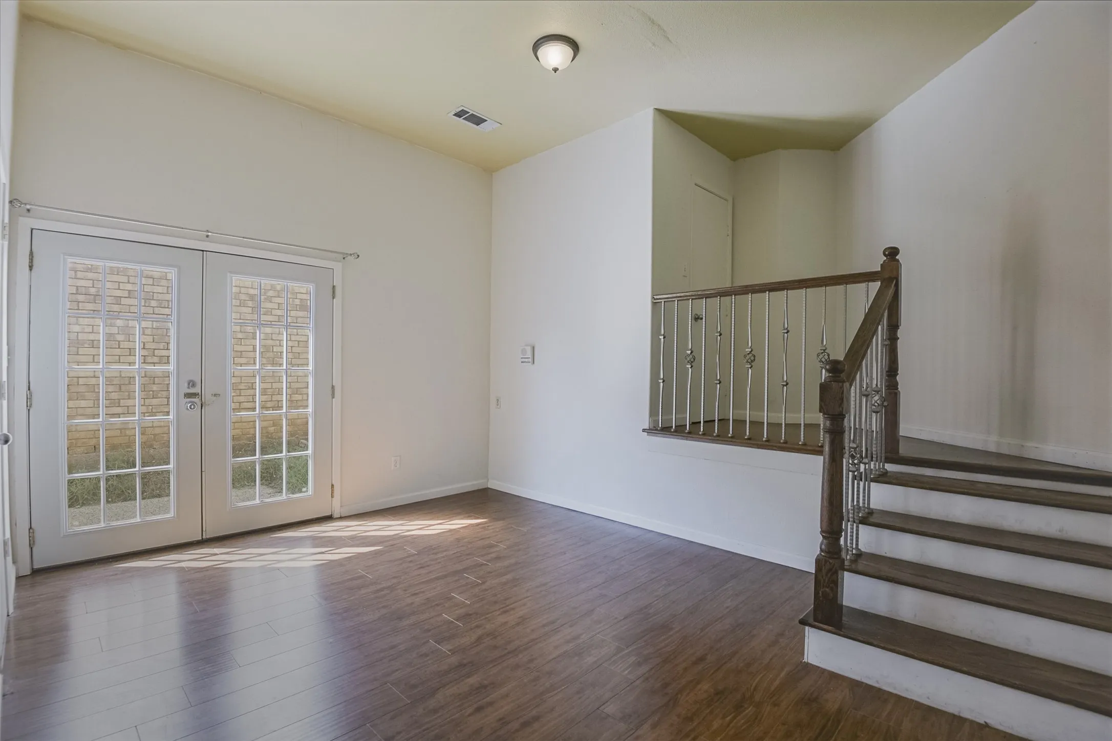 Vaulted ceiling, wood-finish flooring, French doors, wooden staircase with metal balusters, and a recessed wall niche