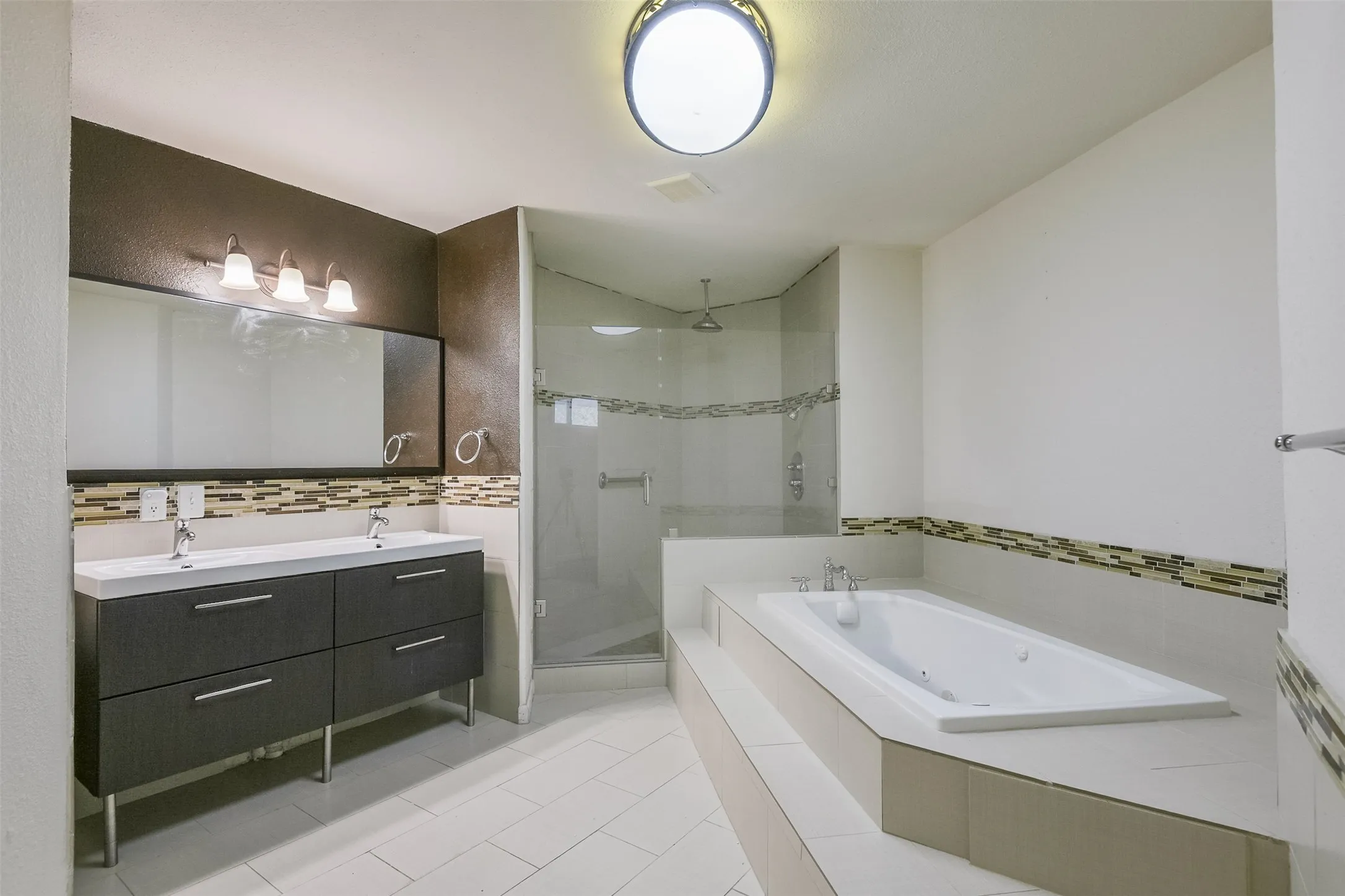 Dual vanity with modern cabinetry, walk-in shower with glass enclosure, built-in soaking tub, and tile flooring