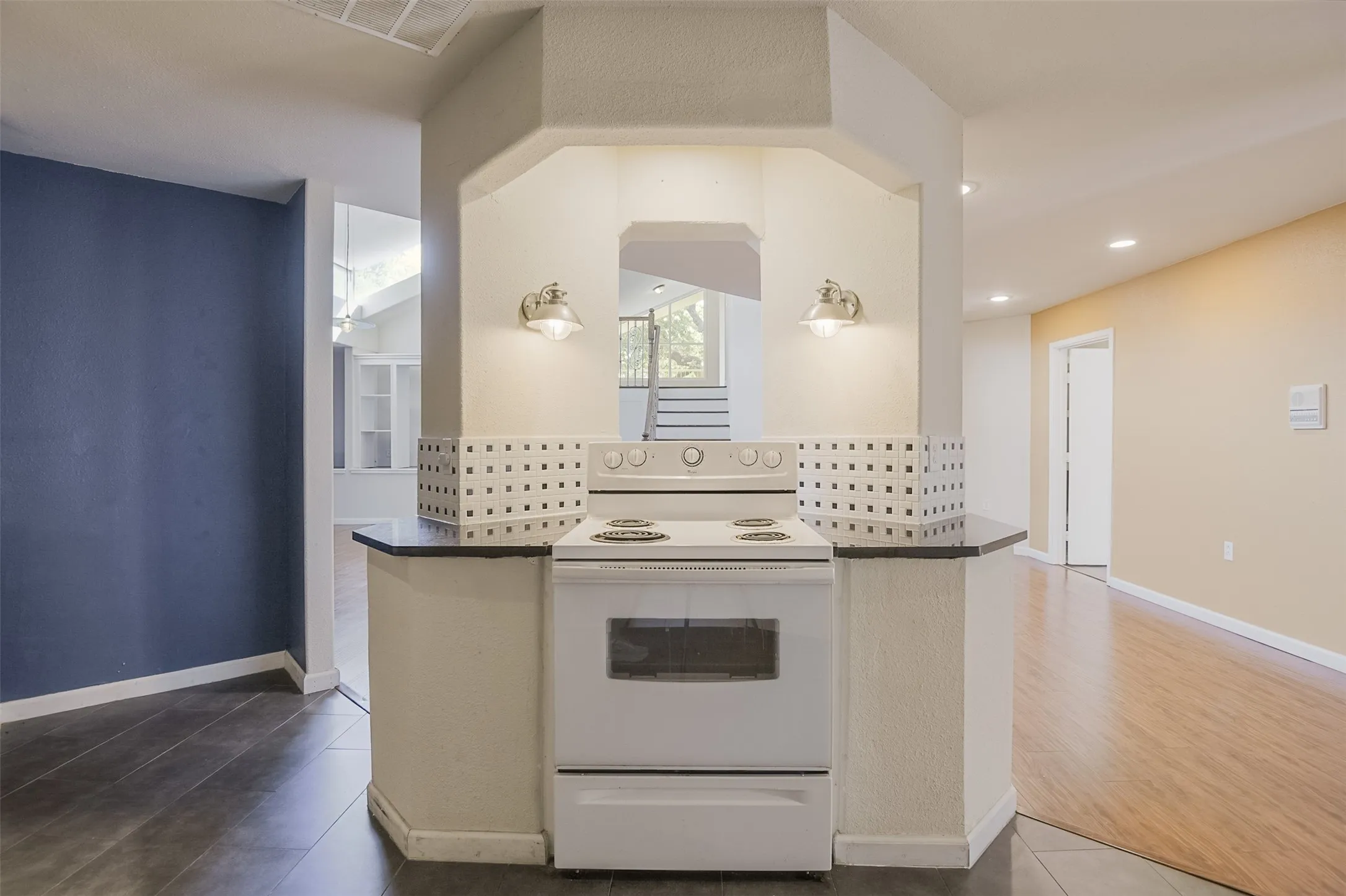 Built-in cooktop with a white finish, black countertops, decorative tile accents, and wall-mounted sconces