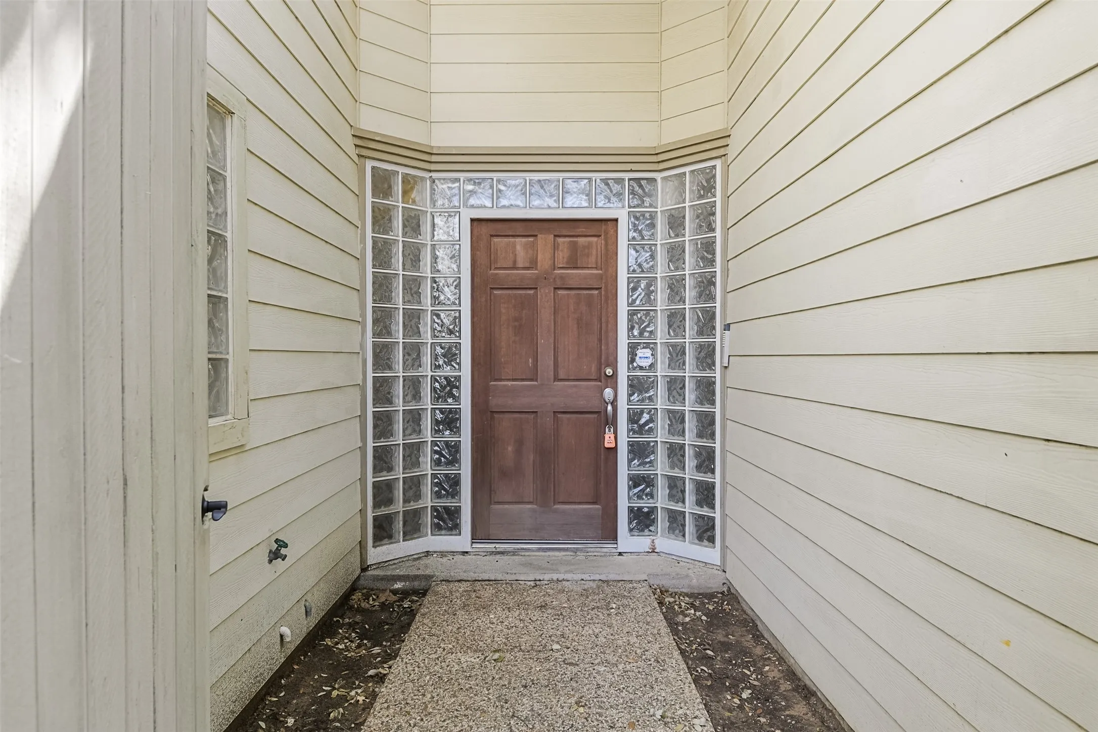 Exterior entry featuring a wood-finish door, glass block sidelights, and light-colored horizontal siding