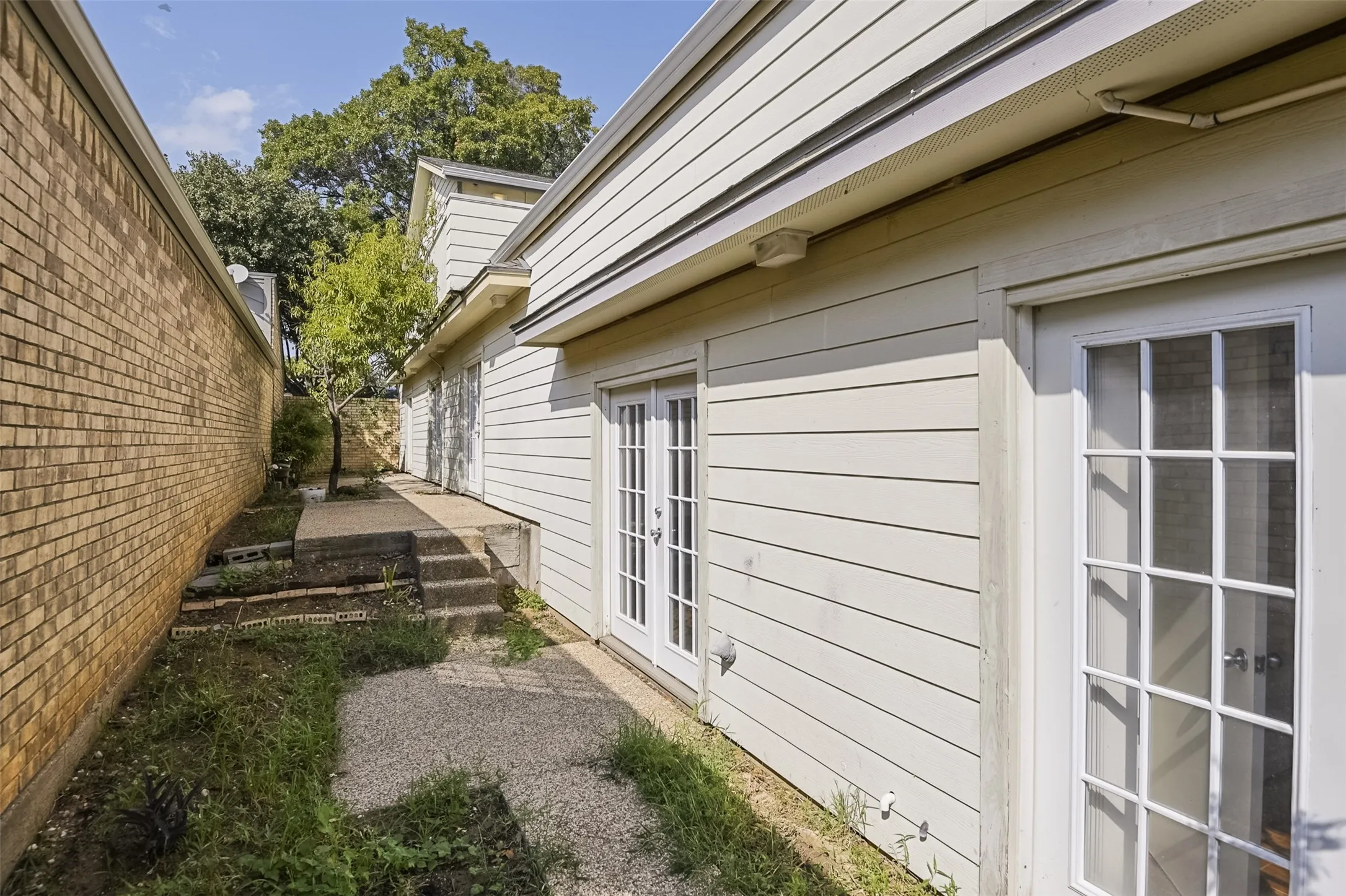 Siding exterior with multiple glass-paneled doors, brick privacy wall, concrete steps, and paved walkway