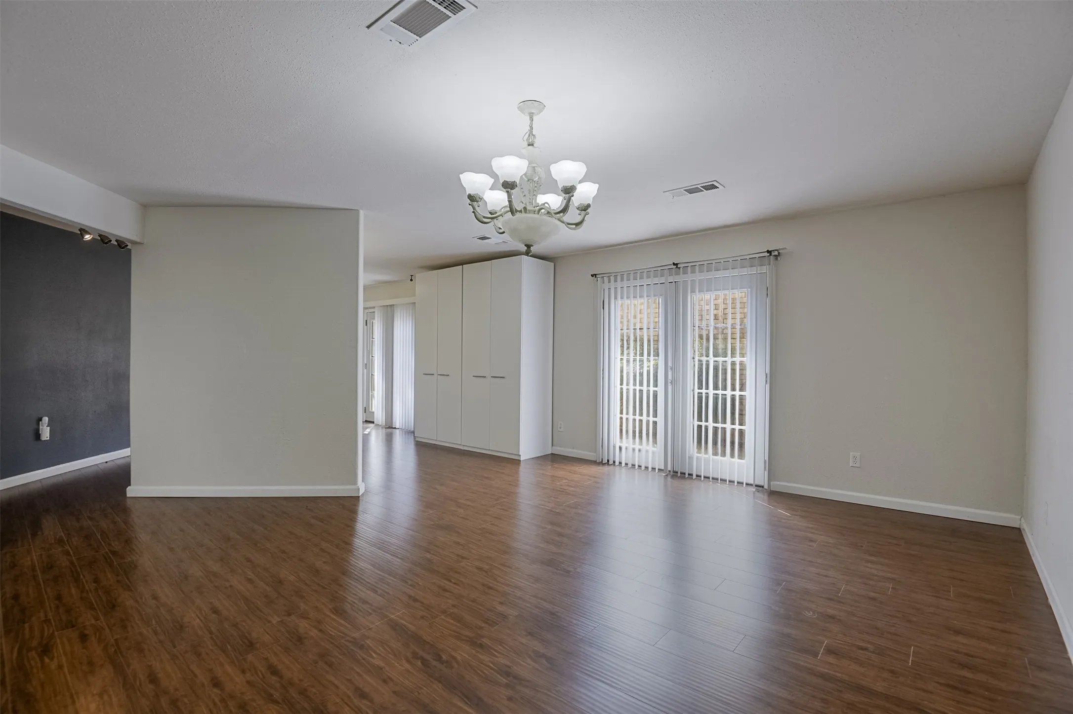 Wood-finish flooring throughout, featuring a multi-bulb chandelier, white built-in cabinetry, and double French doors with vertical blinds