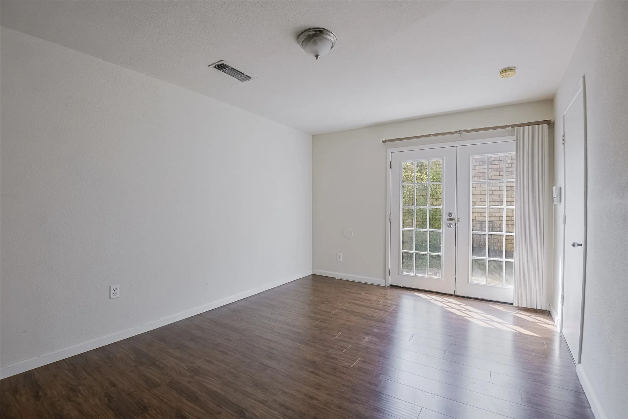Wood-finish flooring, white walls, and white French doors with vertical blinds