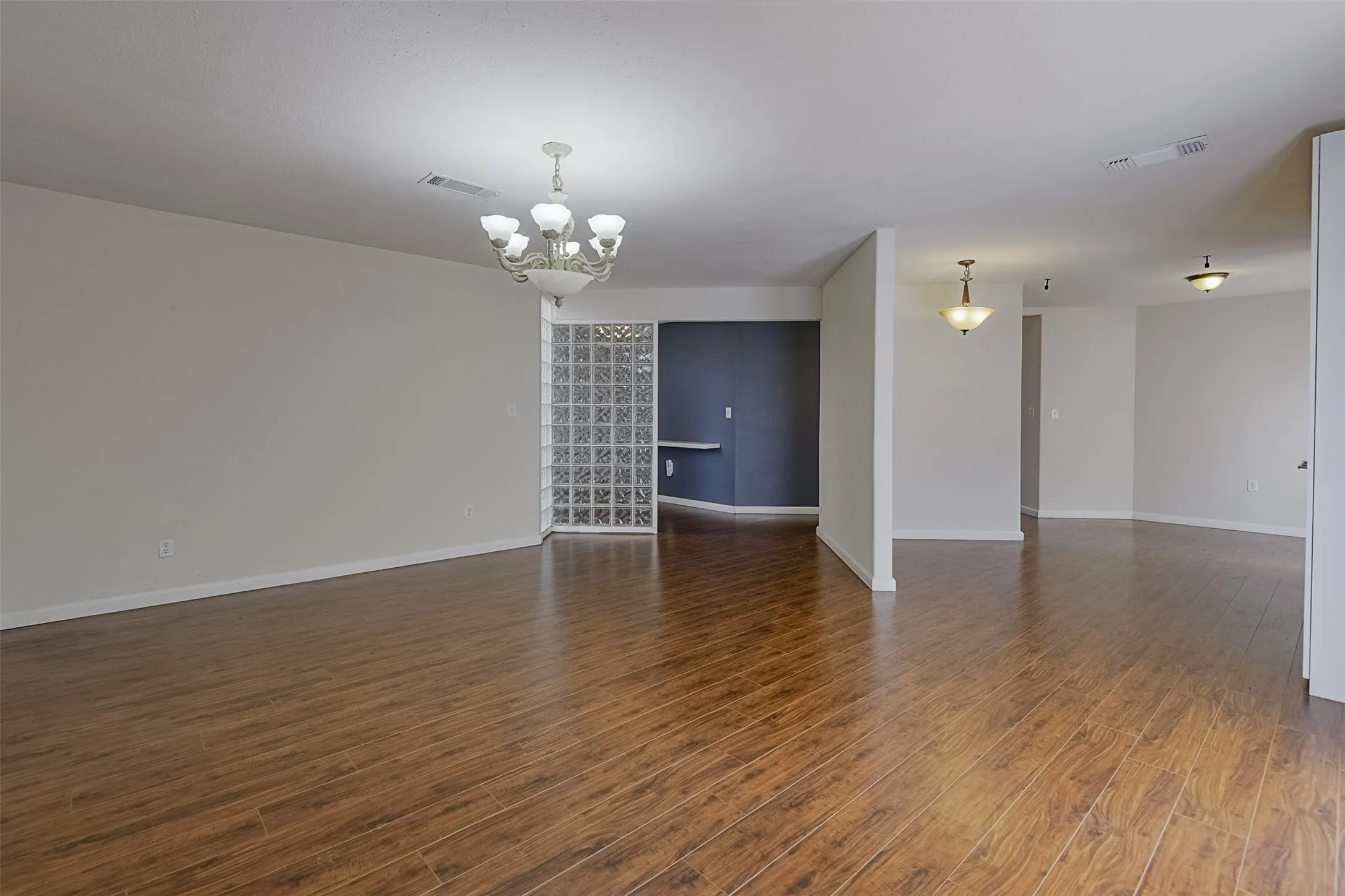 Wood-finish flooring throughout, elegant chandelier, glass block partition, recessed lighting, and modern ceiling fixtures