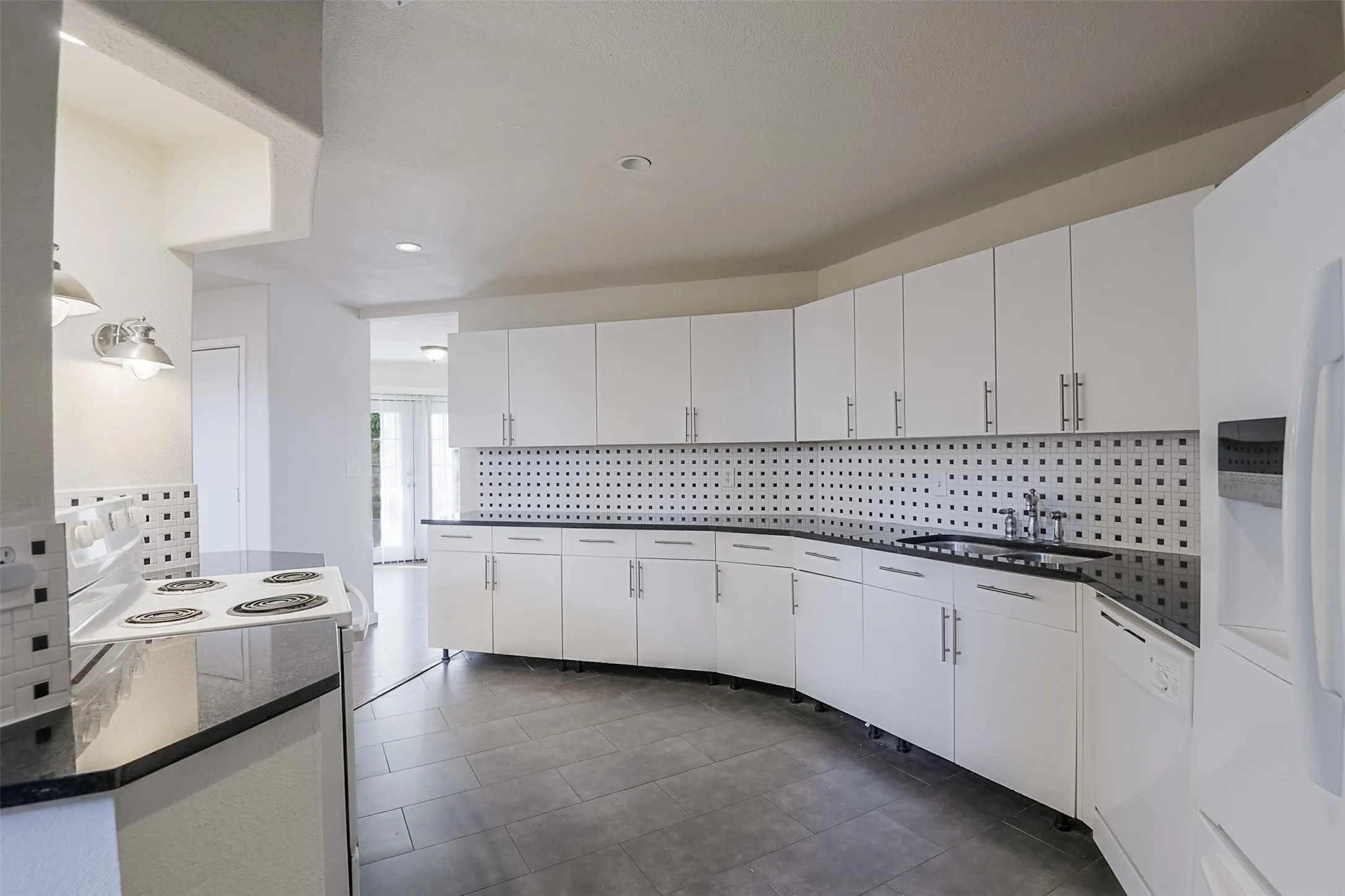 Kitchen featuring extensive white cabinetry, black countertops, a patterned tile backsplash, and tile flooring