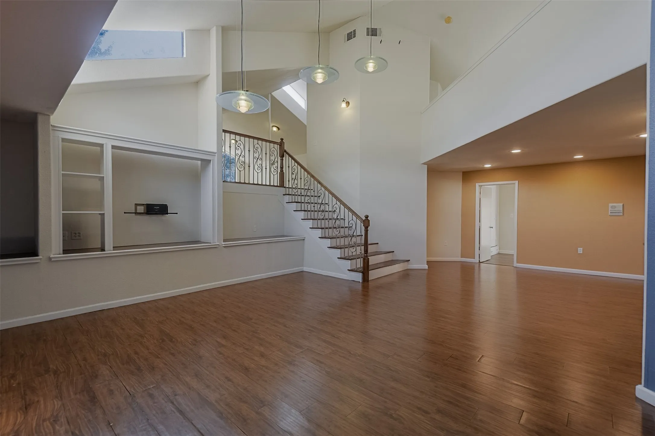 Vaulted ceilings, wood-finish flooring, built-in shelving, staircase with decorative railing, and recessed lighting