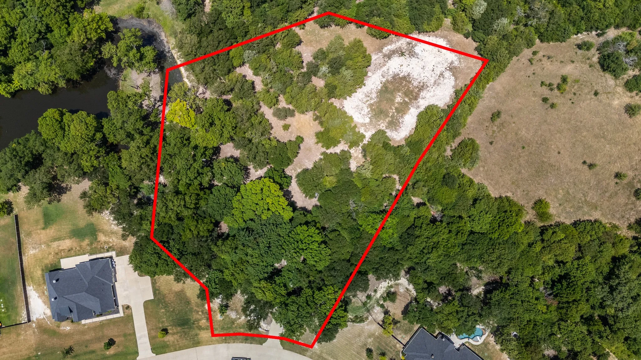 Expansive undeveloped land parcel outlined in red, featuring mature tree coverage, a clearings, and a natural water body along one boundary