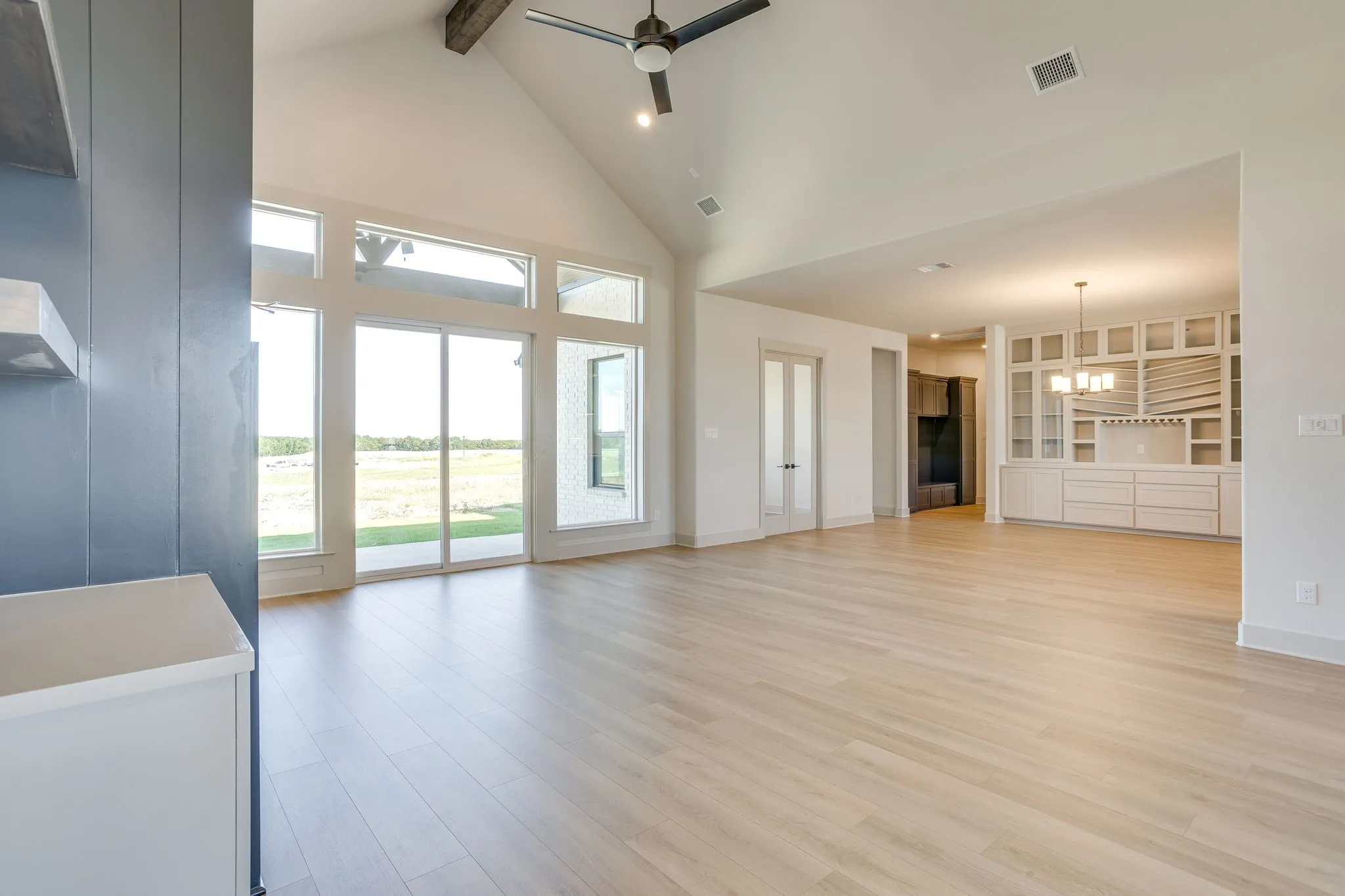 Expansive living area featuring wood-finish flooring, vaulted ceilings with exposed beams, and a ceiling fan