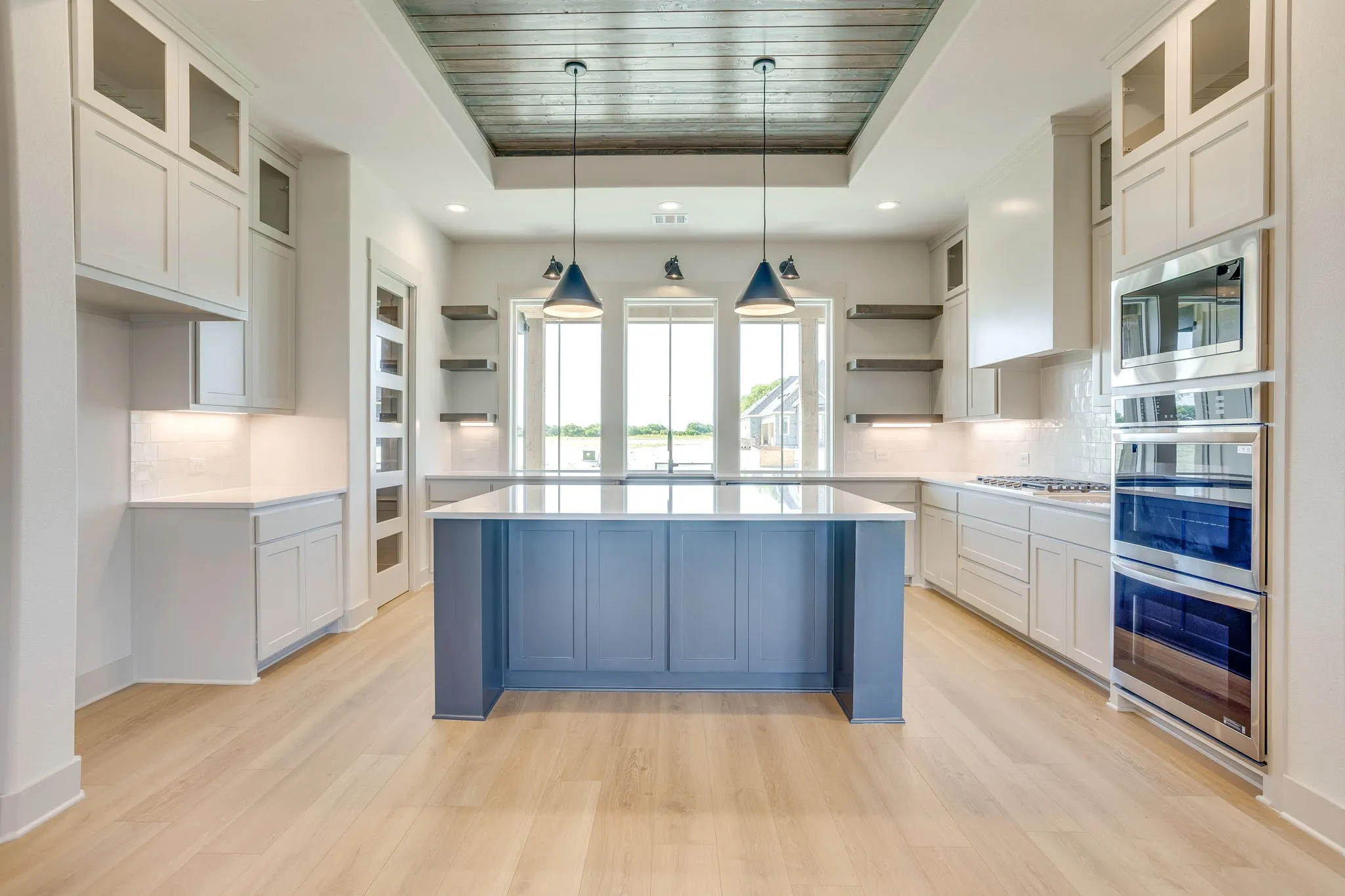Contemporary kitchen featuring a large central island with a blue-painted base, white countertops, and wood-finish flooring