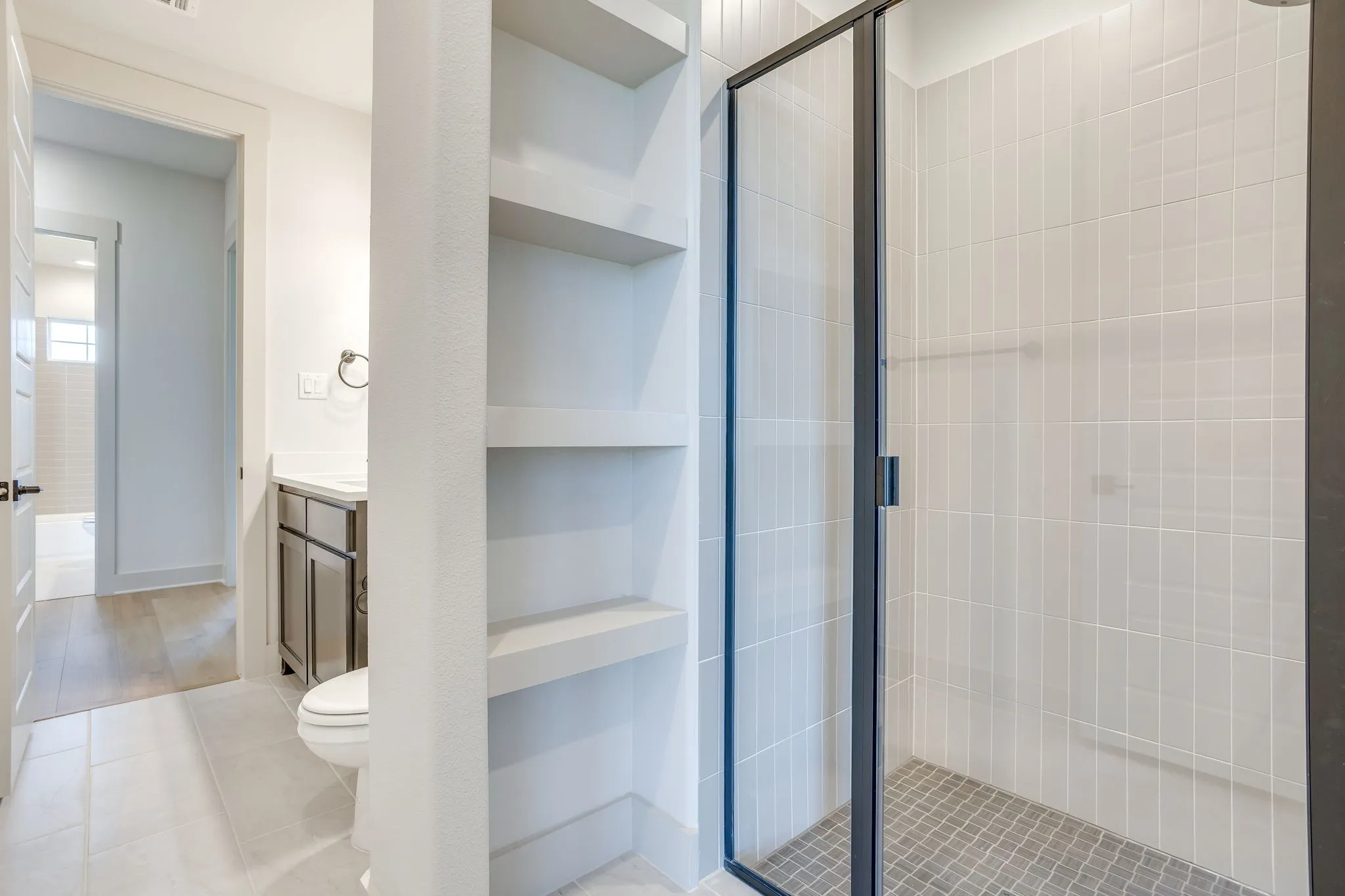 Bathroom featuring a glass-enclosed shower with tiled walls and a mosaic tile floor, built-in shelving, a vanity with a countertop sink, and light-toned floor tiles
