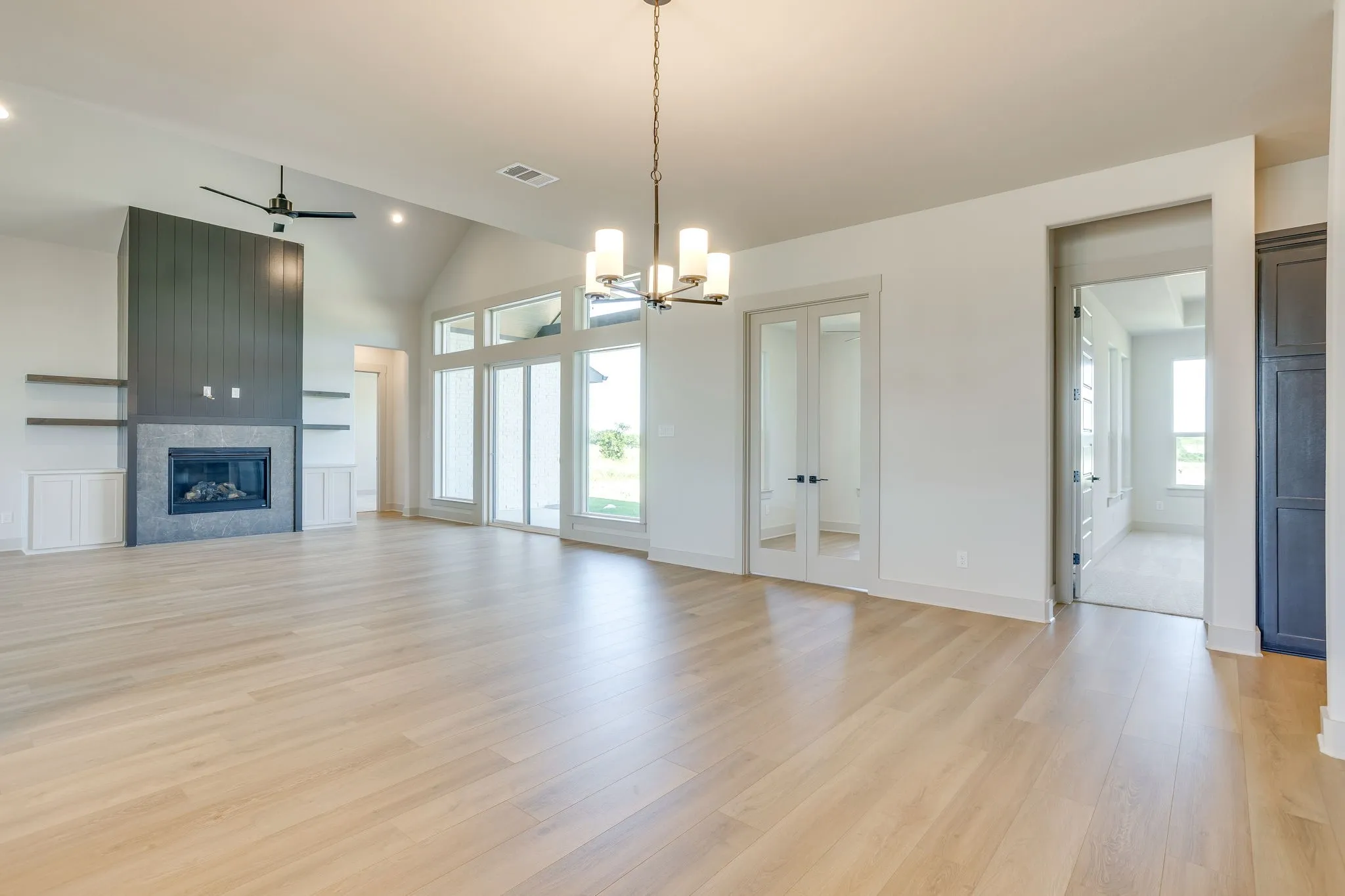 Vaulted ceiling great room featuring wood-finish flooring, a contemporary fireplace with dark shiplap and stone surround, built-in shelving, and a modern chandelier