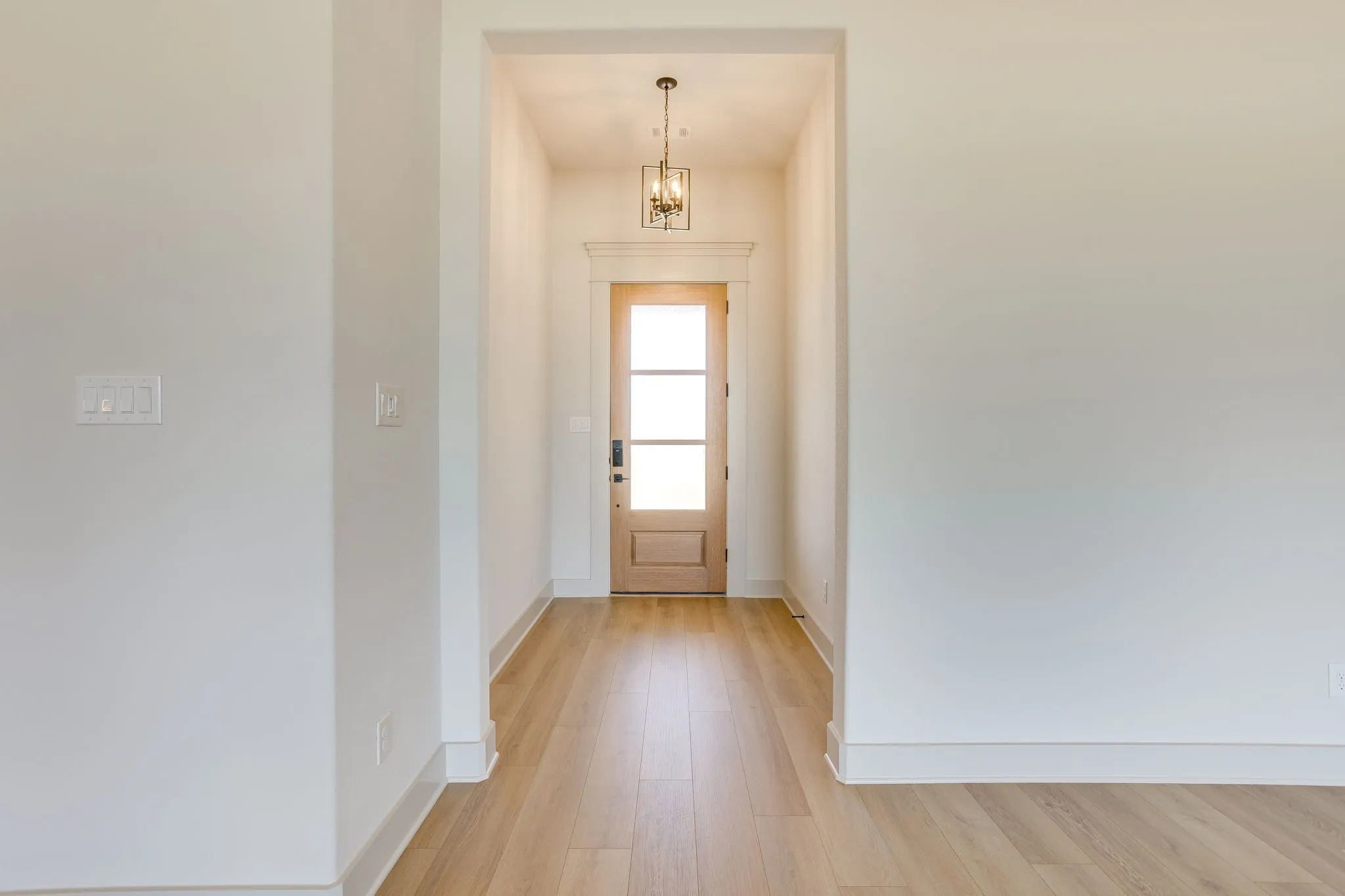 Entryway featuring light wood-finish flooring, a light wood door with glass panes, and a decorative ceiling light fixture