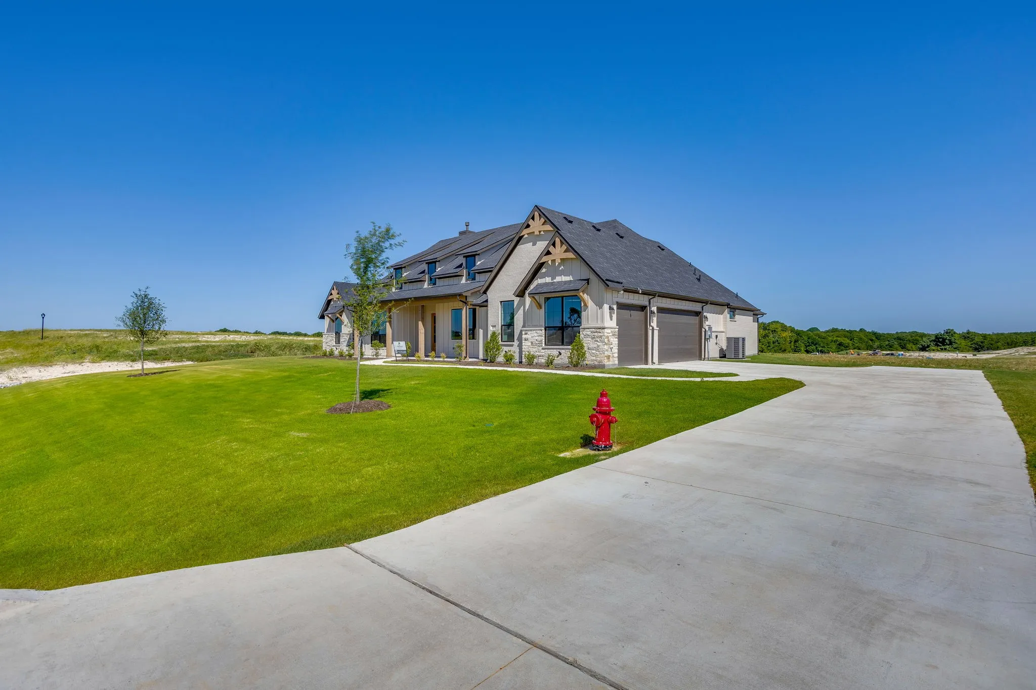 Contemporary exterior featuring light-toned stone and stucco, a dark shingle roof, decorative wood gable accents, and a covered entry