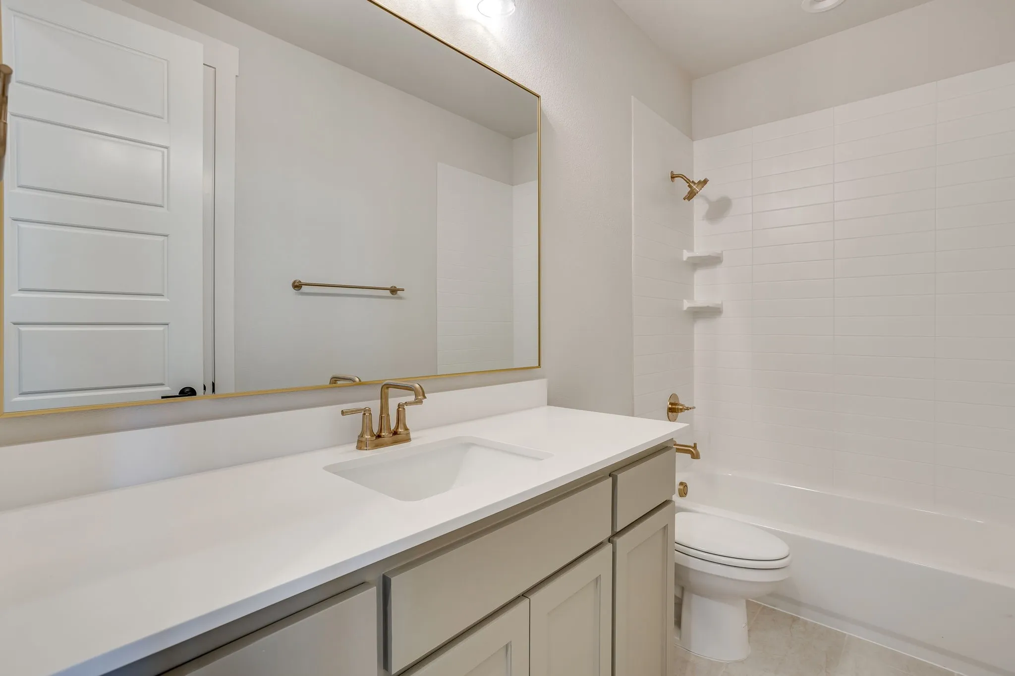 Bathroom featuring a single vanity with an integrated sink, light-toned cabinetry, and a full-width mirror with a gold-toned frame
