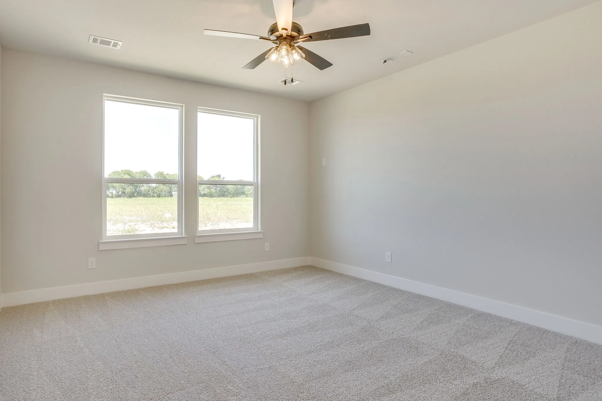 Spacious room featuring neutral carpeting, two large windows, a ceiling fan with integrated lighting, and crown molding