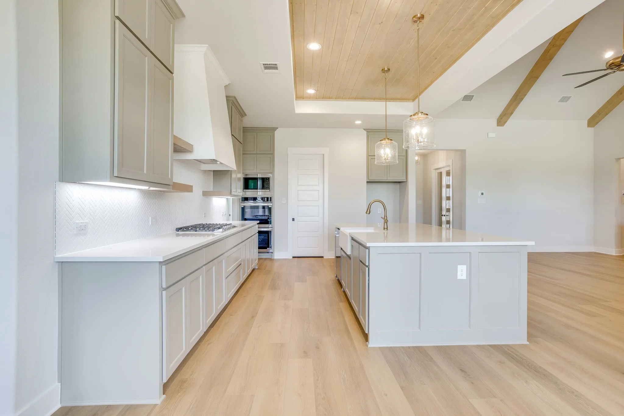 Gourmet kitchen featuring a central island with an integrated farmhouse sink, light wood-finish flooring, white countertops, gray cabinetry, and a subway tile backsplash