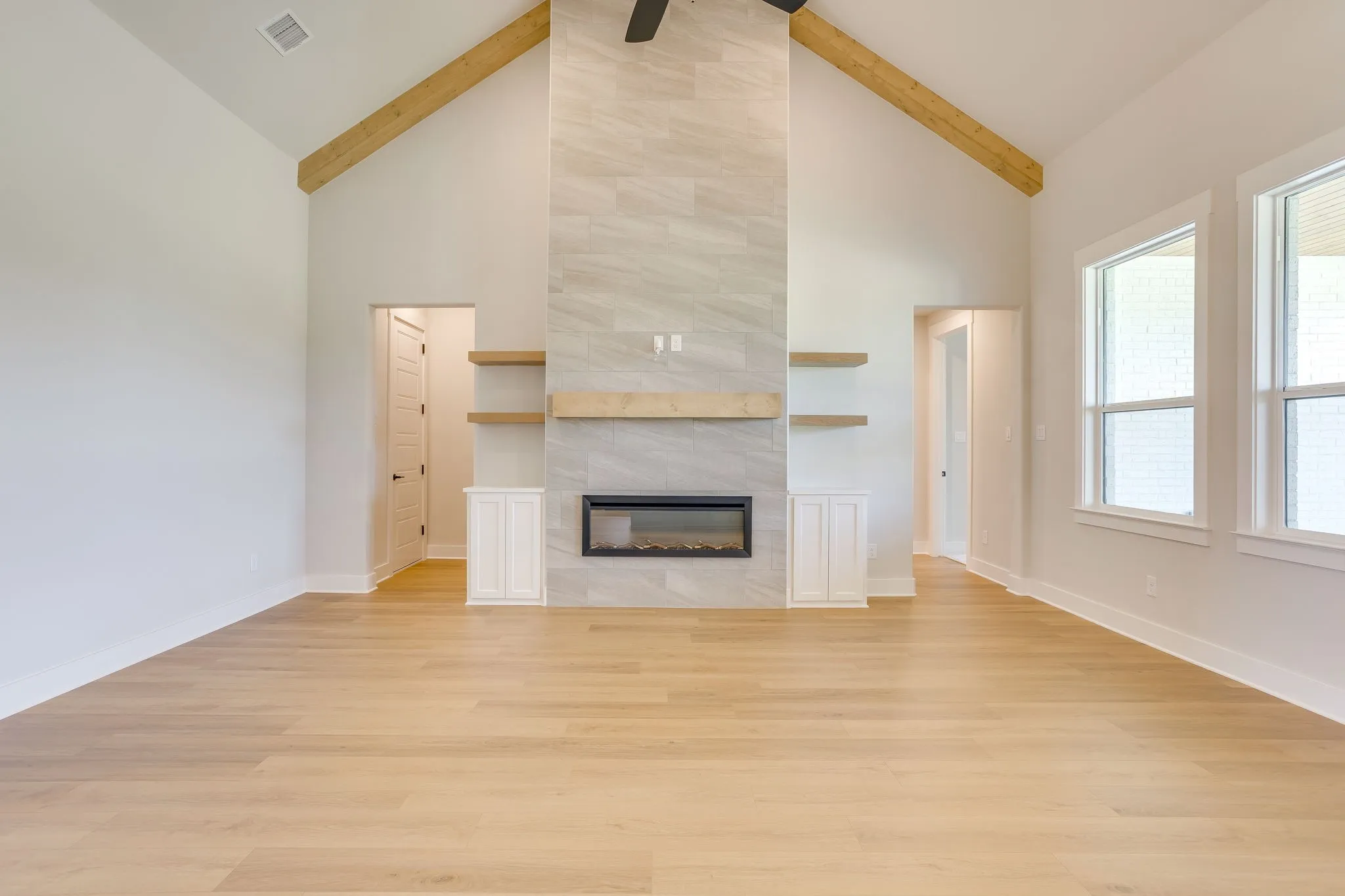 Vaulted living space featuring a tiled fireplace with an electric insert, wood-finish mantel, and built-in shelving and cabinetry