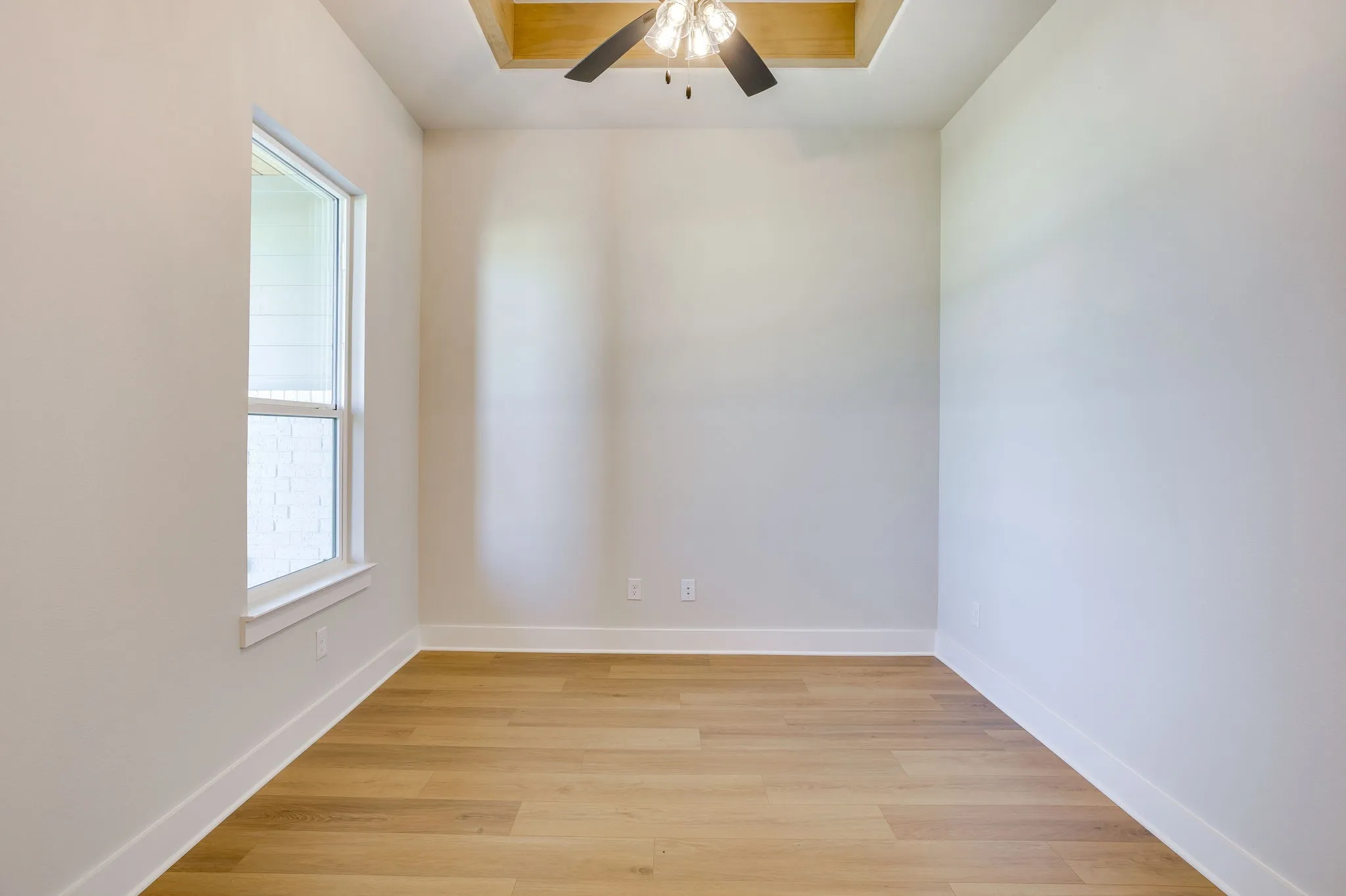 Recessed ceiling with wood-finish trim and a ceiling fan, light wood-finish flooring, white baseboards, and a double-hung window
