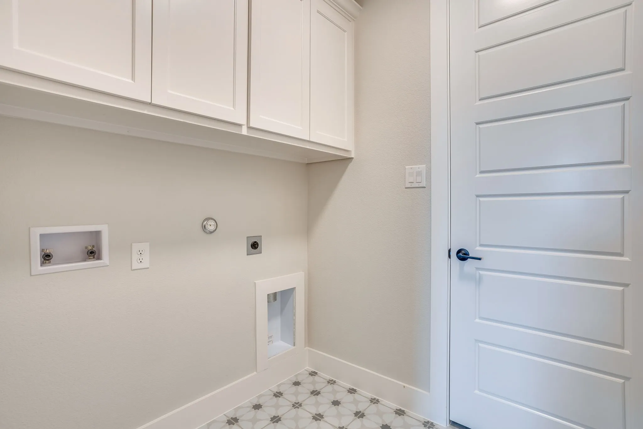 Utility area featuring white shaker-style cabinetry, patterned floor tiling, and a contrasting black door handle