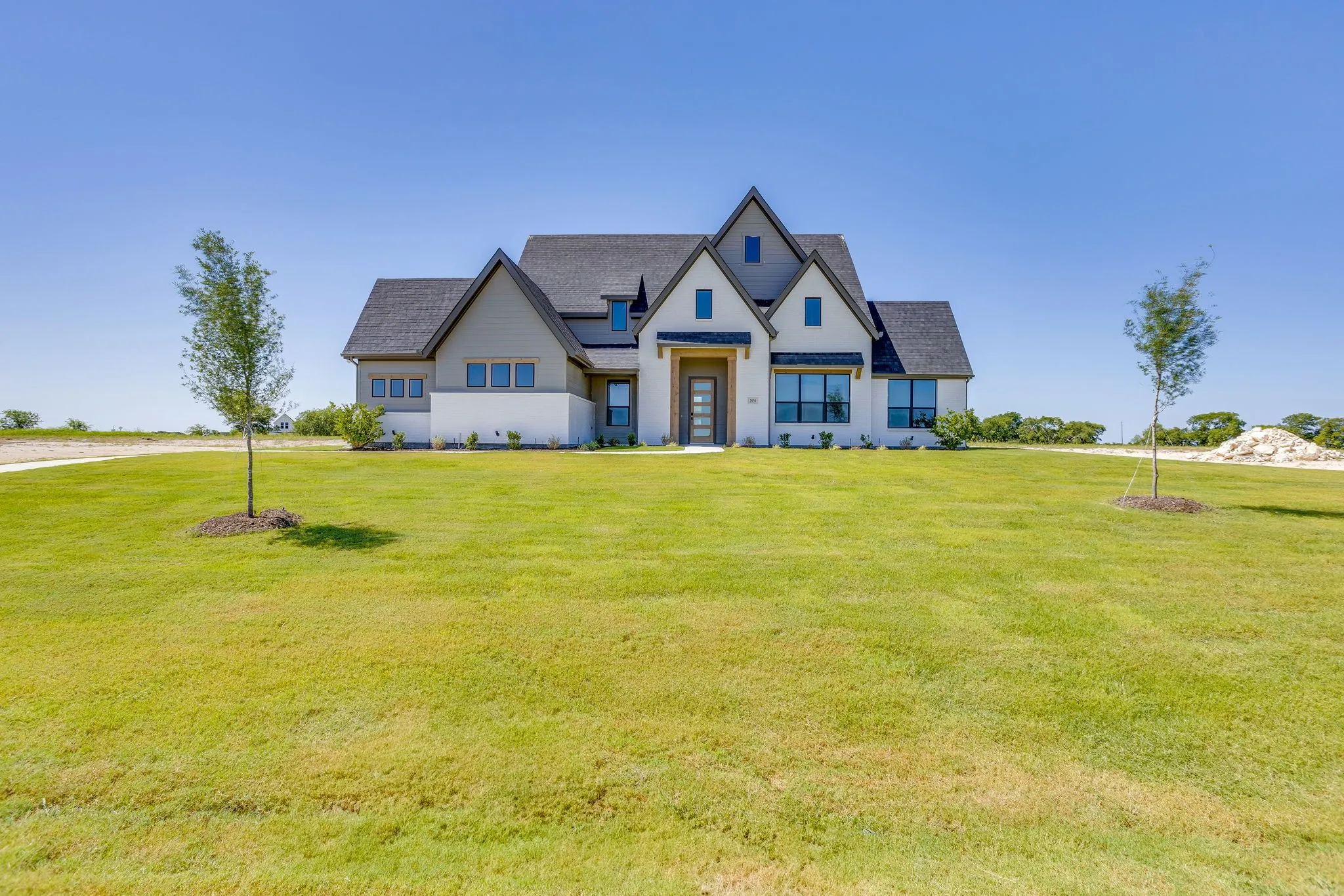 Modern farmhouse exterior featuring a dark asphalt shingle roof, light grey siding, white brick, and a prominent front entry with a wood-finish door