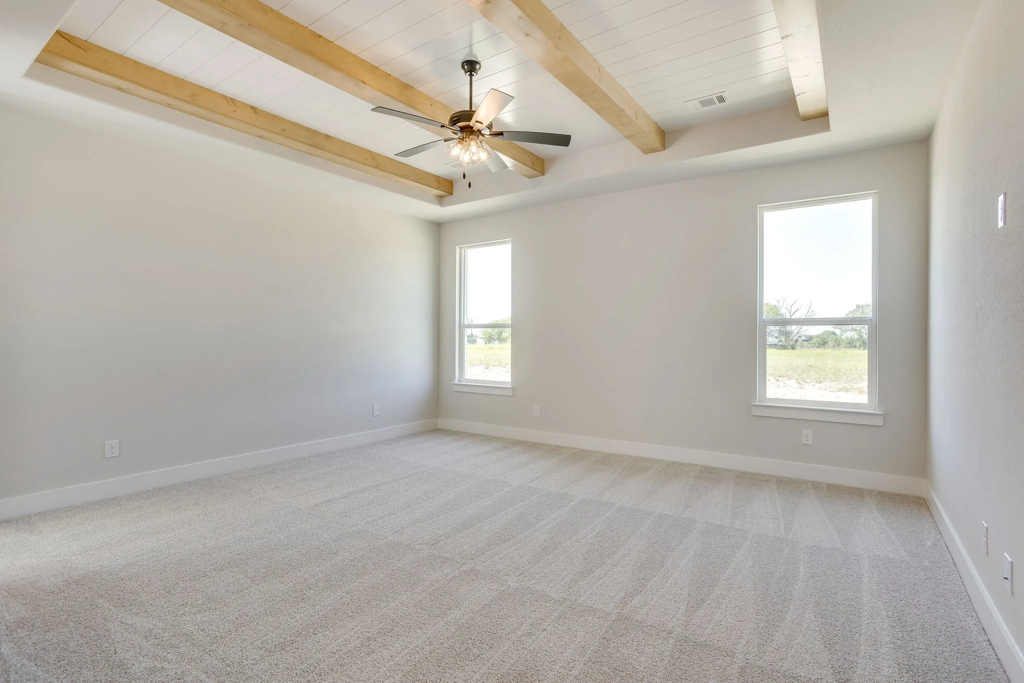 Spacious room featuring a tray ceiling with wood-finish beams, a ceiling fan, and light gray carpeting