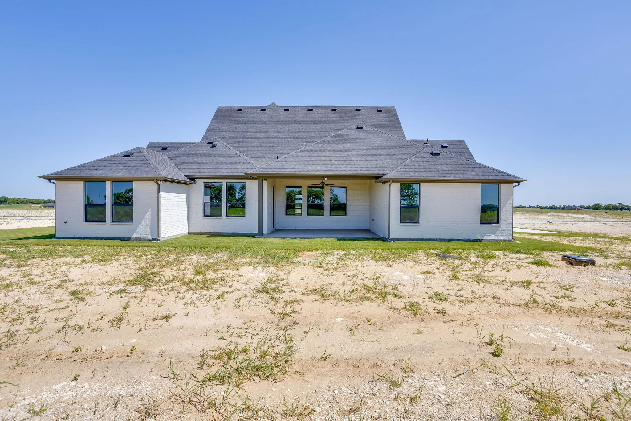 Rear exterior featuring a covered patio, multiple large windows with dark frames, and a dark shingle roofline