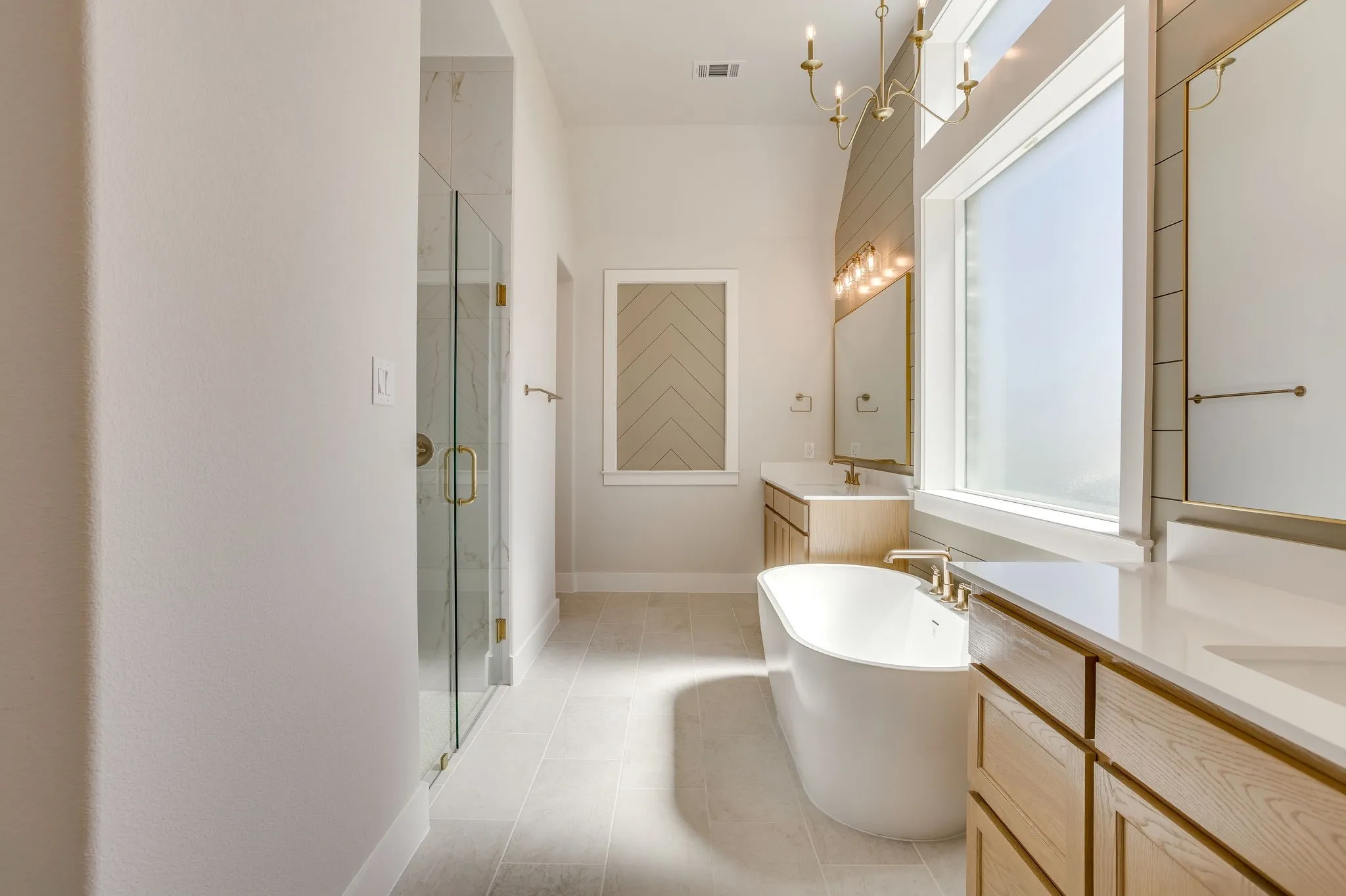 Contemporary bathroom featuring a freestanding tub, dual vanities with light wood-finish cabinetry, and a glass-enclosed shower