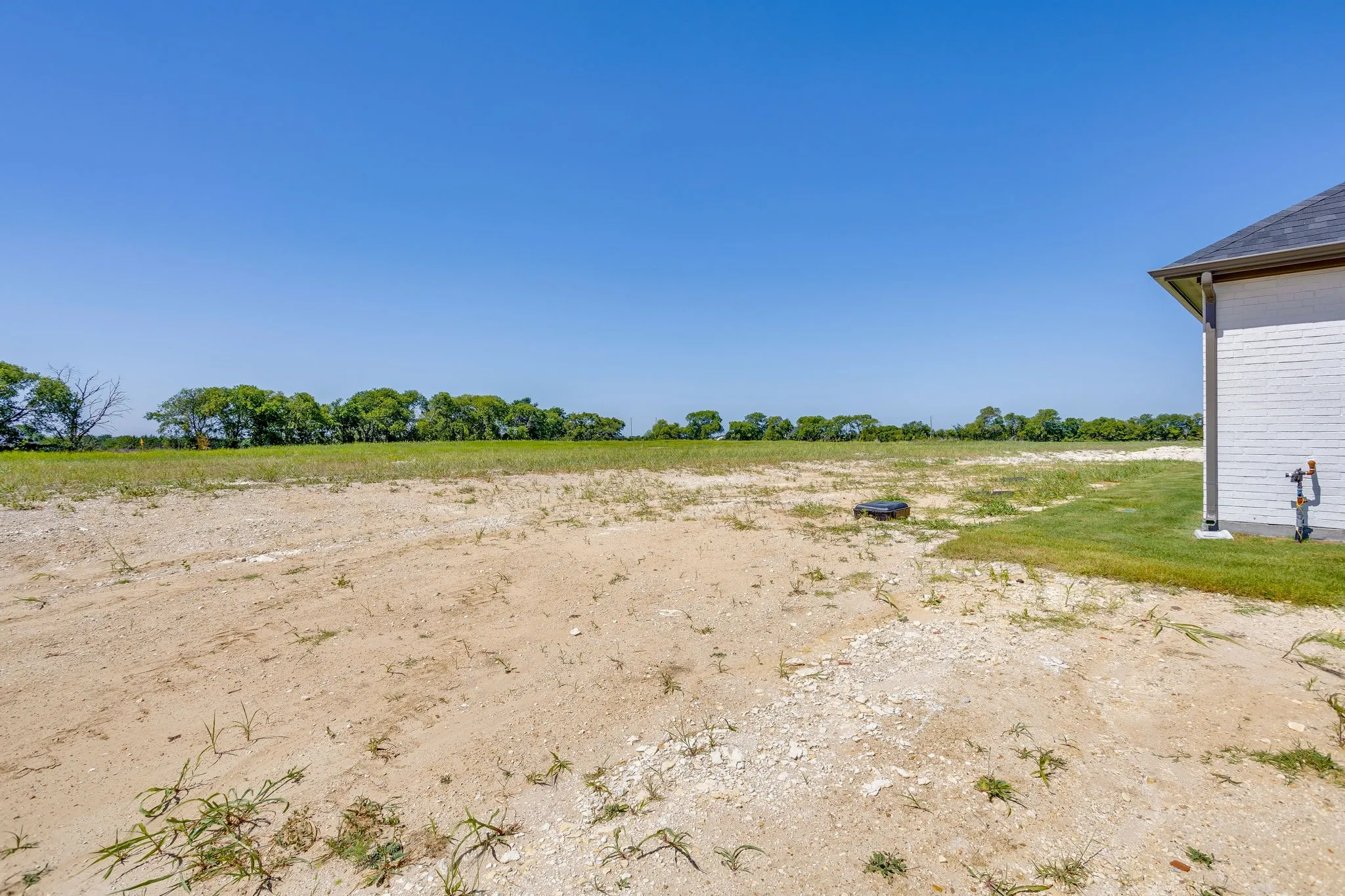 Expansive undeveloped lot featuring a partially graded surface, a section of turfgrass, and a white brick exterior